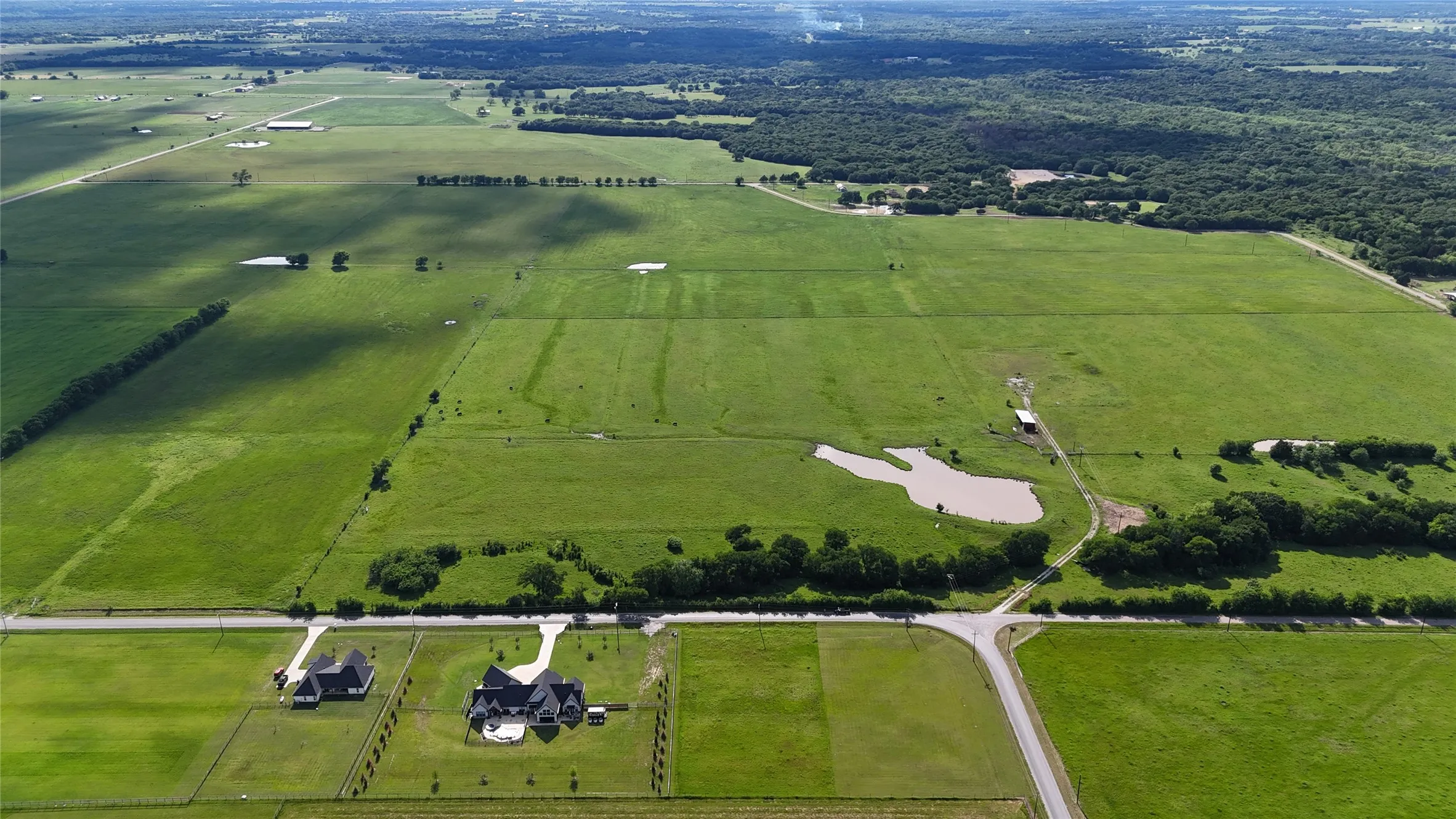 Expansive green pastures featuring a private pond, scattered trees, and distant wooded areas
