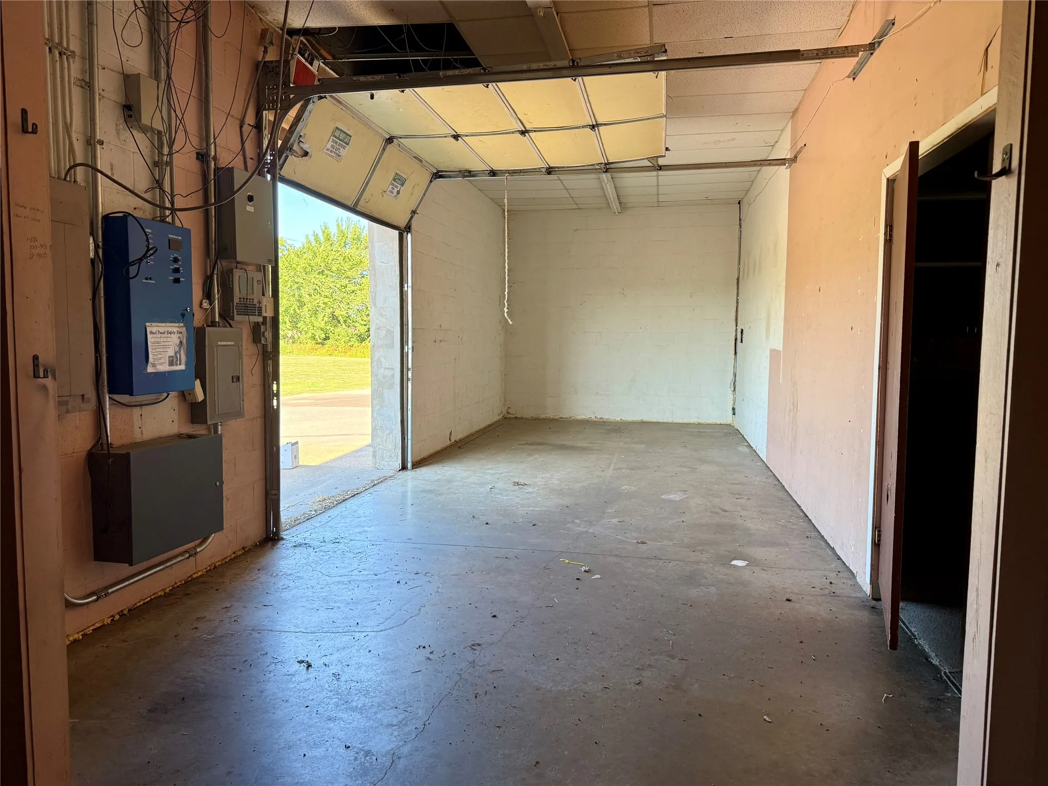 Interior workshop space featuring a concrete floor, overhead garage door, exposed ceiling joists, and multiple electrical panels