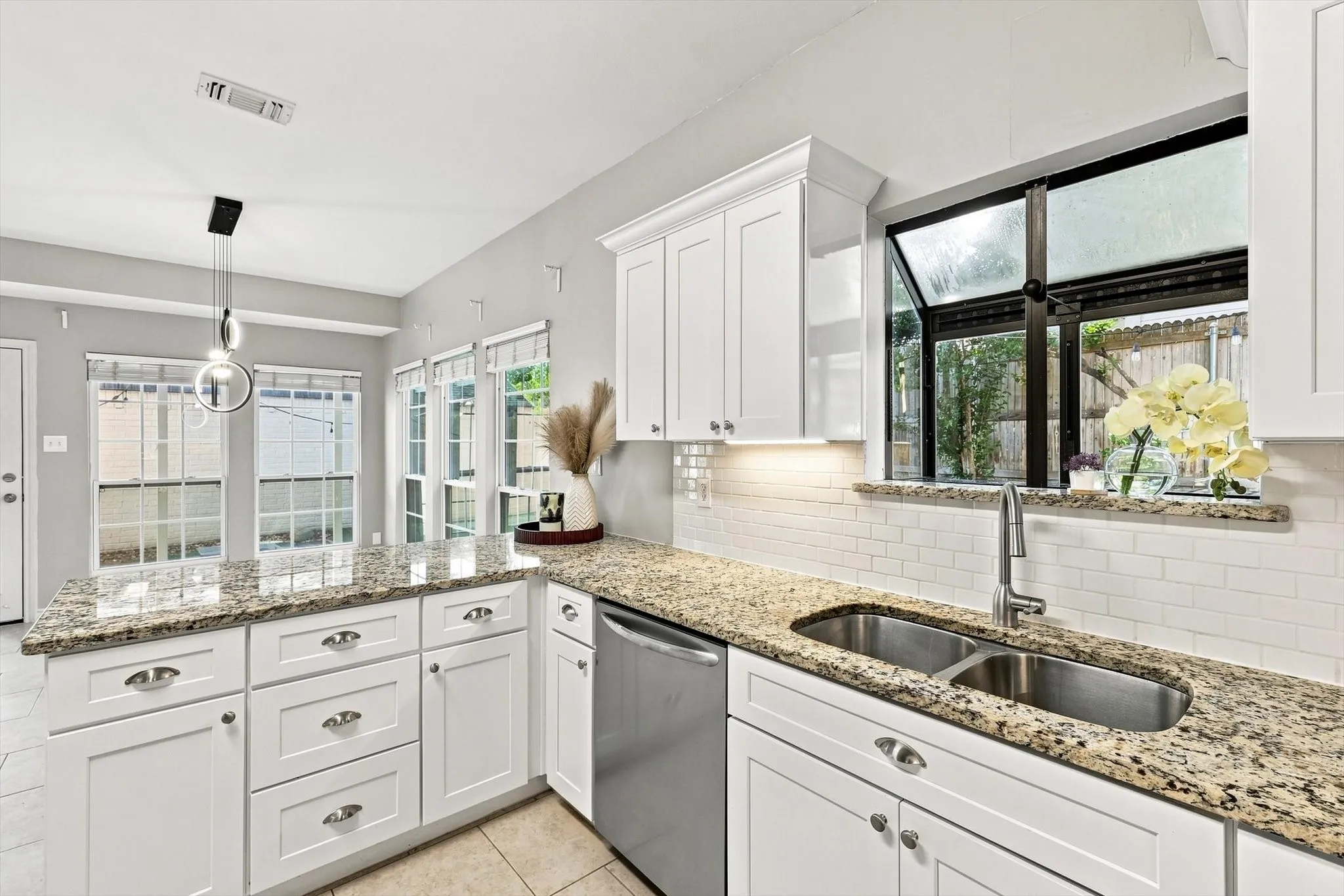 White shaker-style cabinetry, granite countertops, subway tile backsplash, stainless steel double basin sink, and a modern pendant light fixture