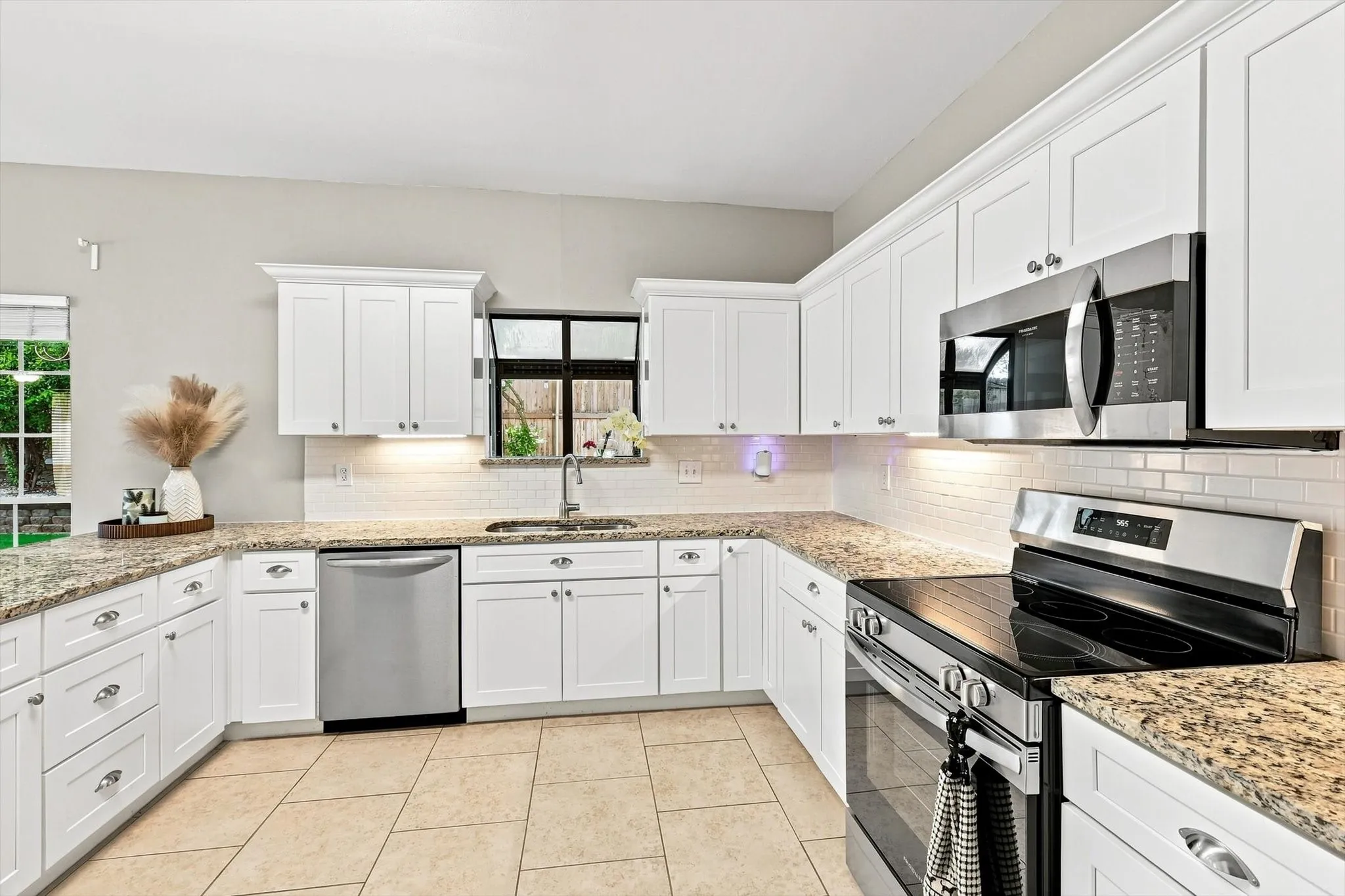 White cabinetry, stainless steel appliances, speckled stone countertops, subway tile backsplash, and tile flooring