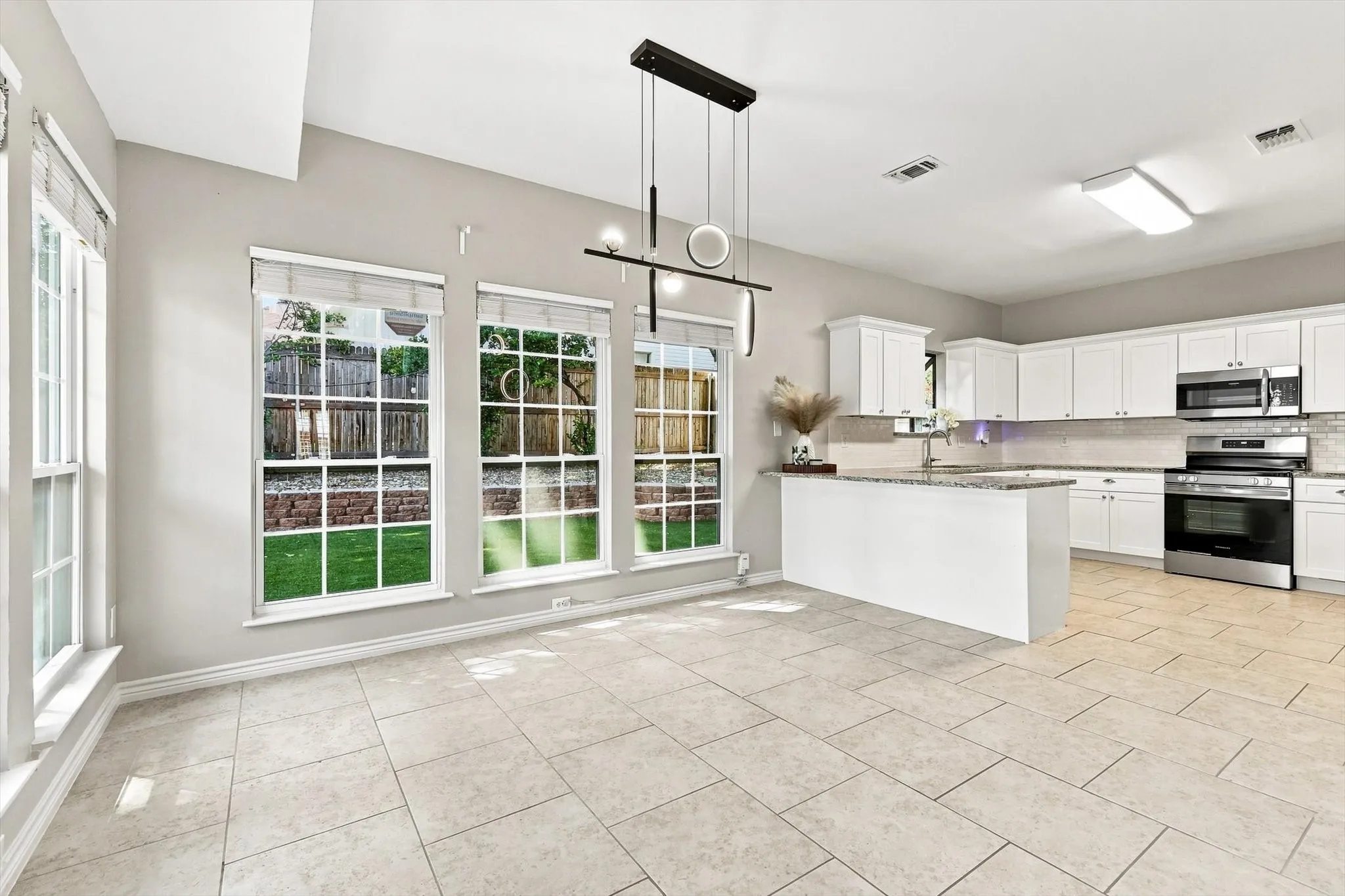 Open-concept kitchen and dining area featuring white cabinetry, stainless steel appliances, a center island with a granite-style countertop, and large windows