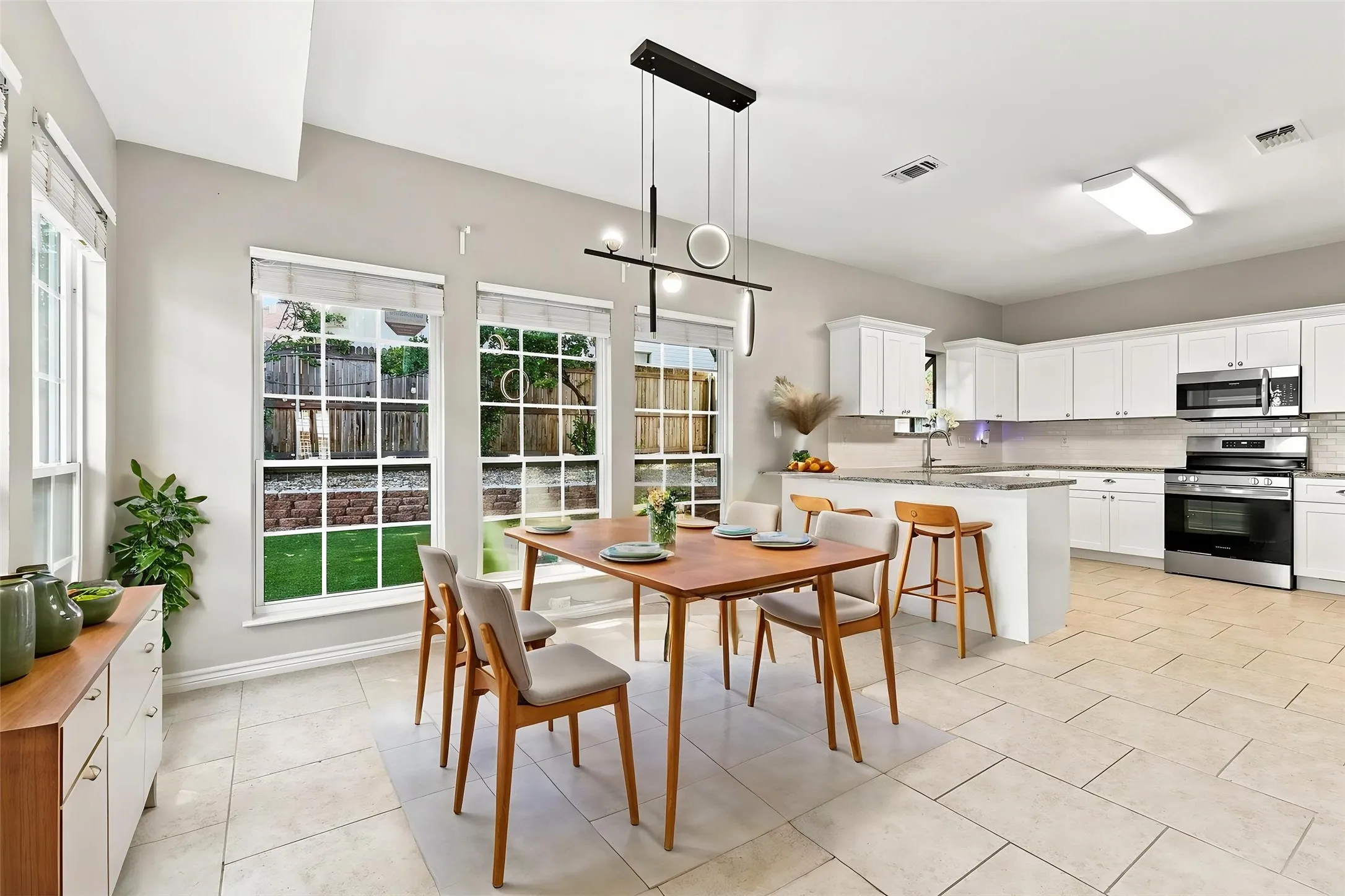 Kitchen and dining area featuring a contemporary island with bar seating, stainless steel appliances, white cabinetry, and large windows