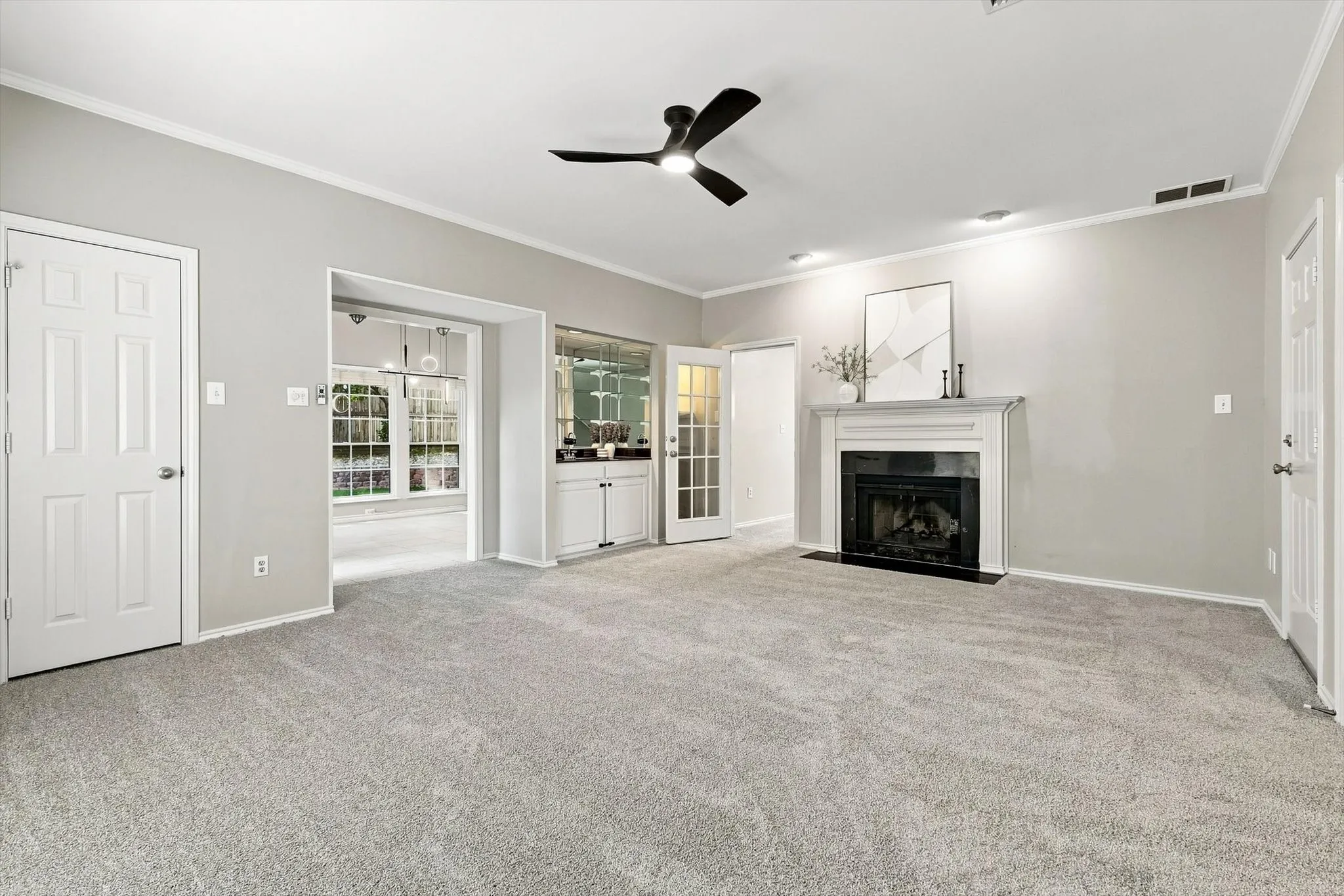 Neutral tone wall paint, light gray carpeting, ceiling fan, built-in cabinetry with mirrored backsplash, and a fireplace with a white mantel