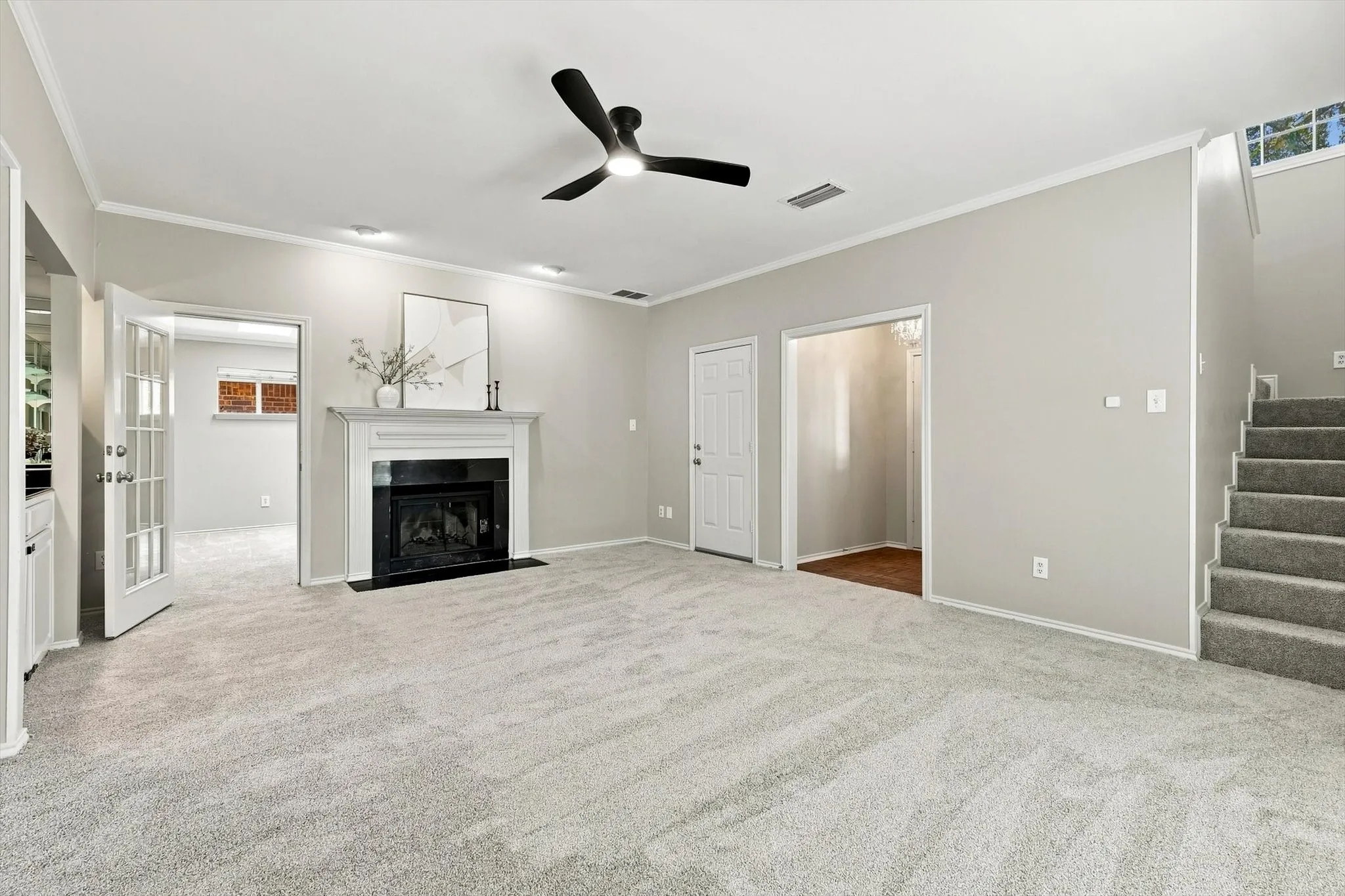 Spacious open-concept living area featuring neutral carpet flooring, a ceiling fan with dark blades, and a fireplace with black surround and mantel