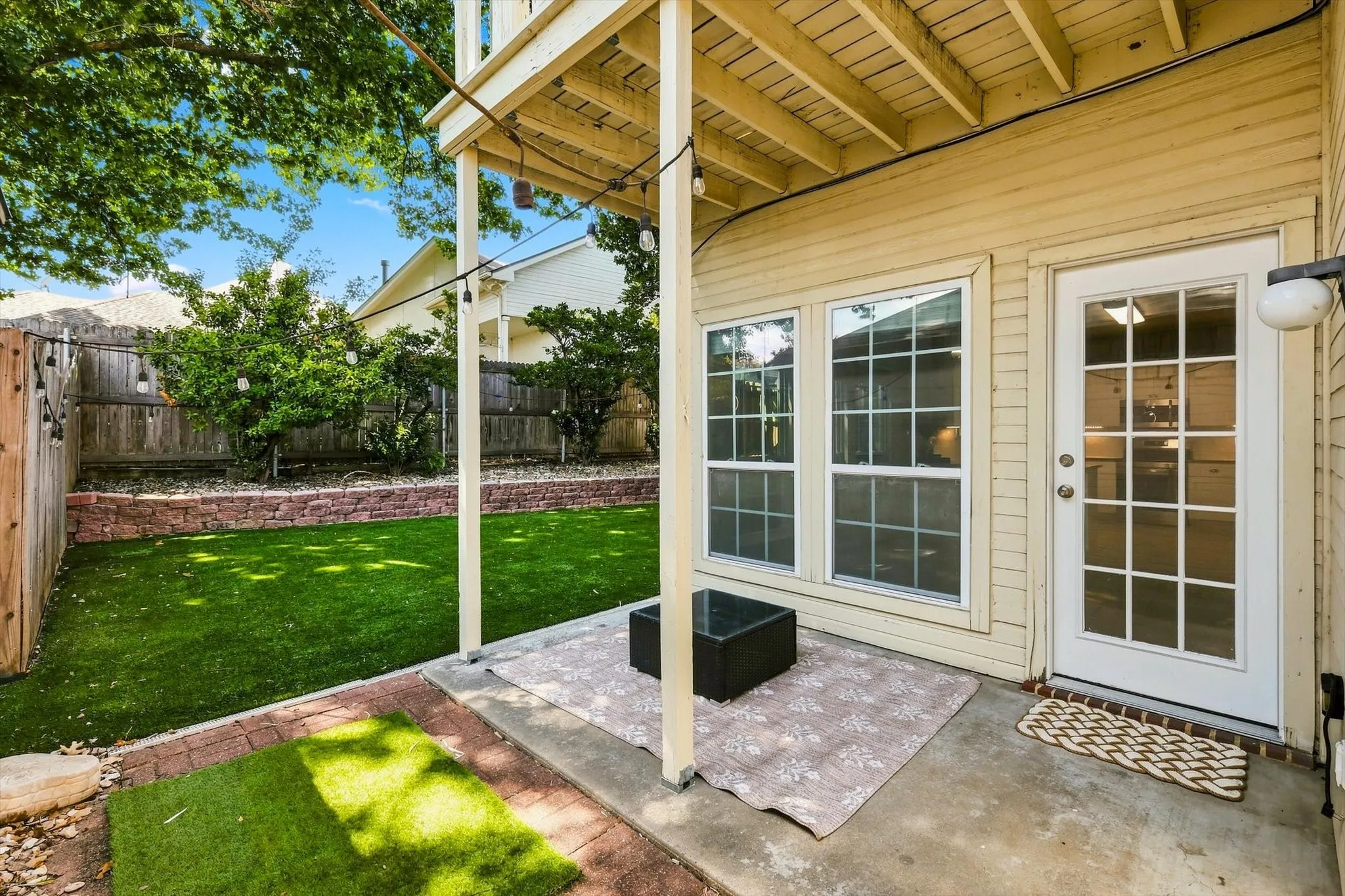 Covered patio with concrete and brick paver flooring, multiple windows, and a glass-paneled door