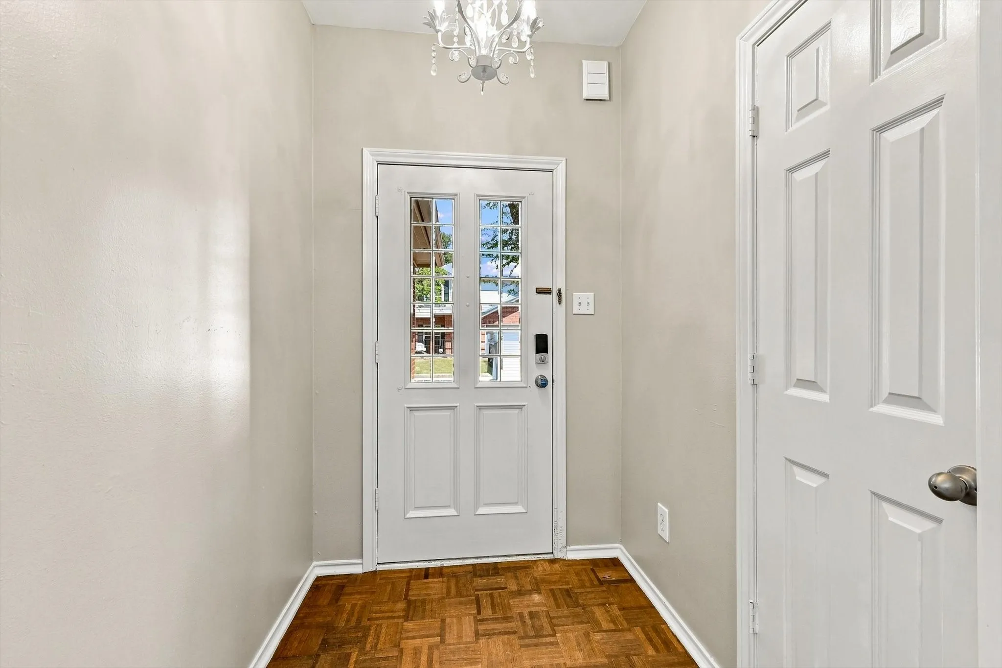 Entryway featuring a white paneled front door with glass inserts, wood-finish flooring, a white interior door, and a chandelier