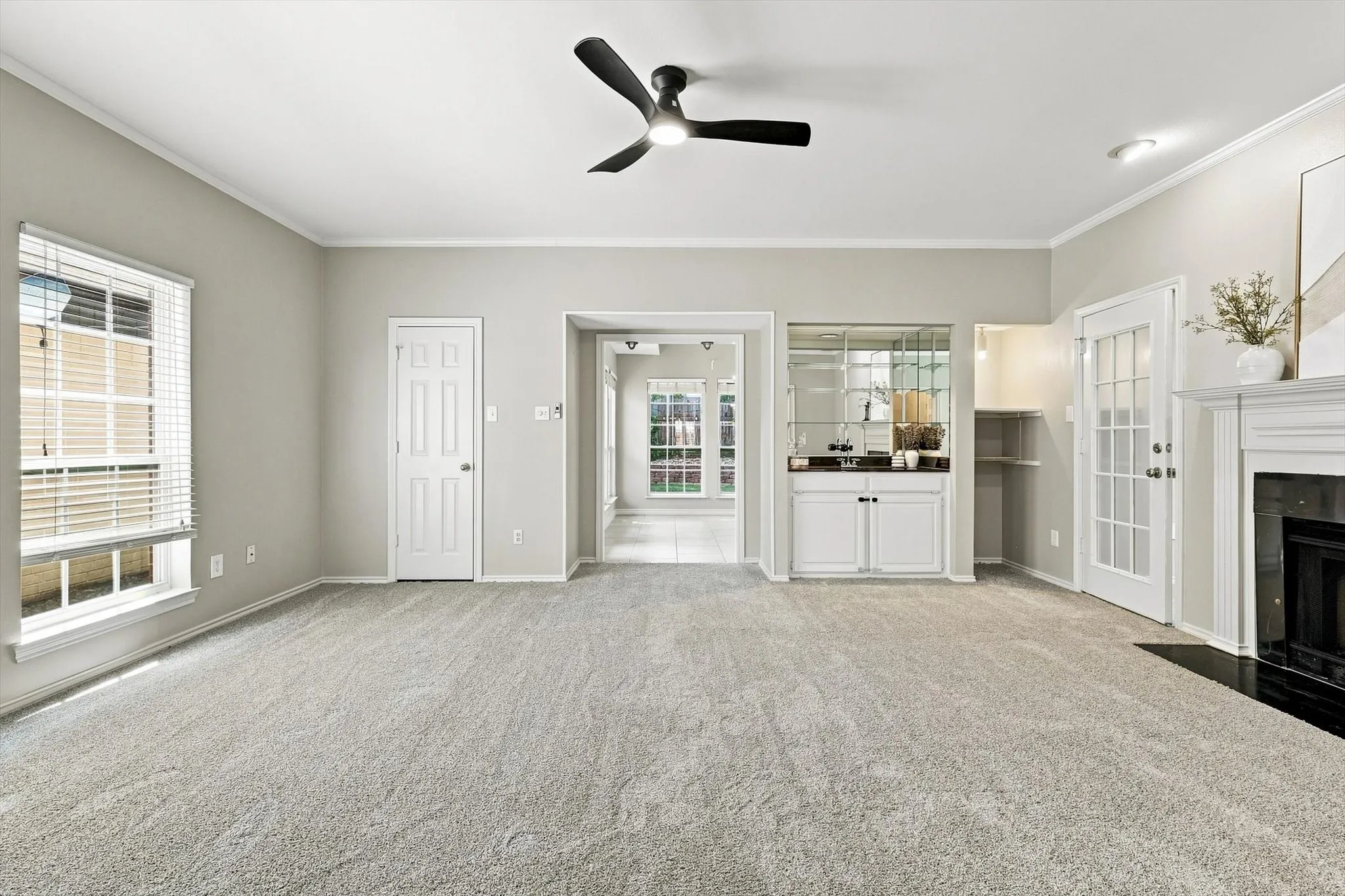 Living area featuring light gray carpeting, a contemporary black ceiling fan, and a built-in wet bar with mirrored backsplash