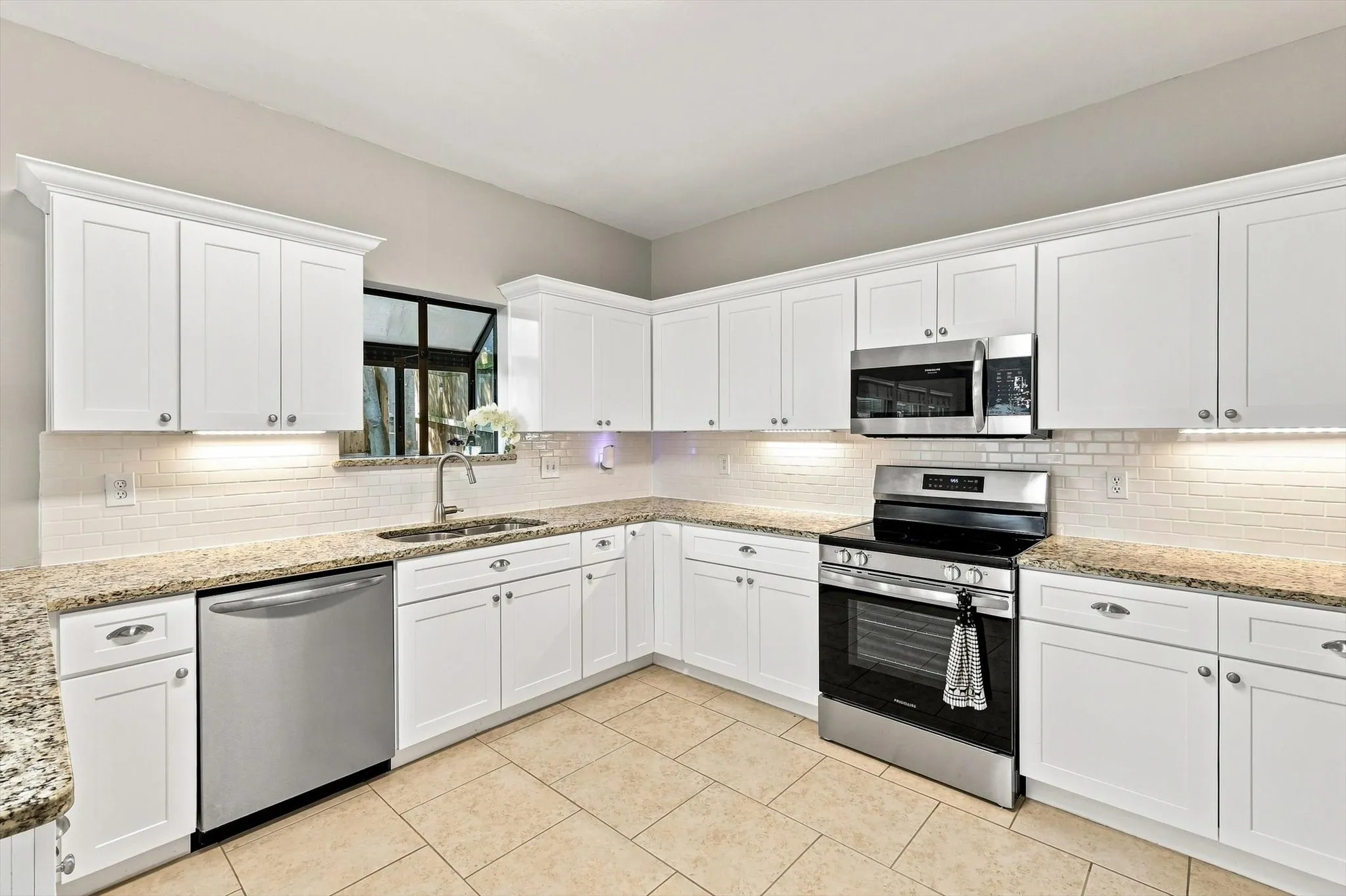 Kitchen with white shaker cabinetry, light-toned tiled flooring, granite countertops, stainless steel appliances, and a subway tile backsplash