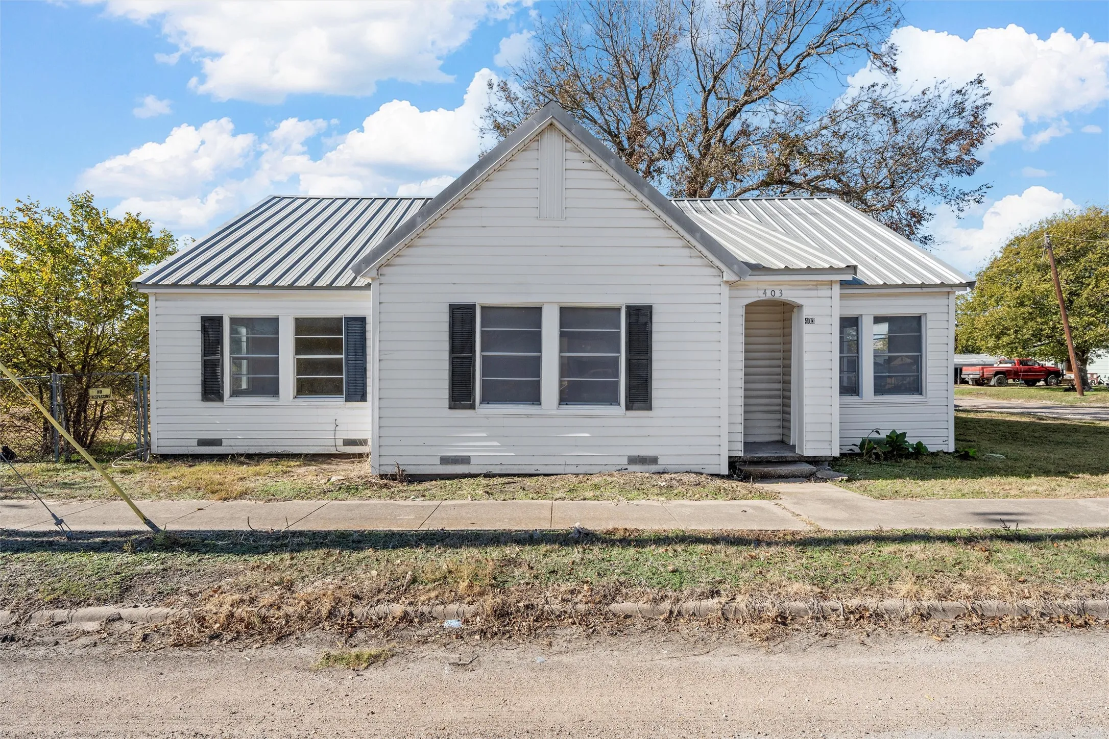 White siding residence featuring a corrugated metal roof, black window shutters, and a covered entry