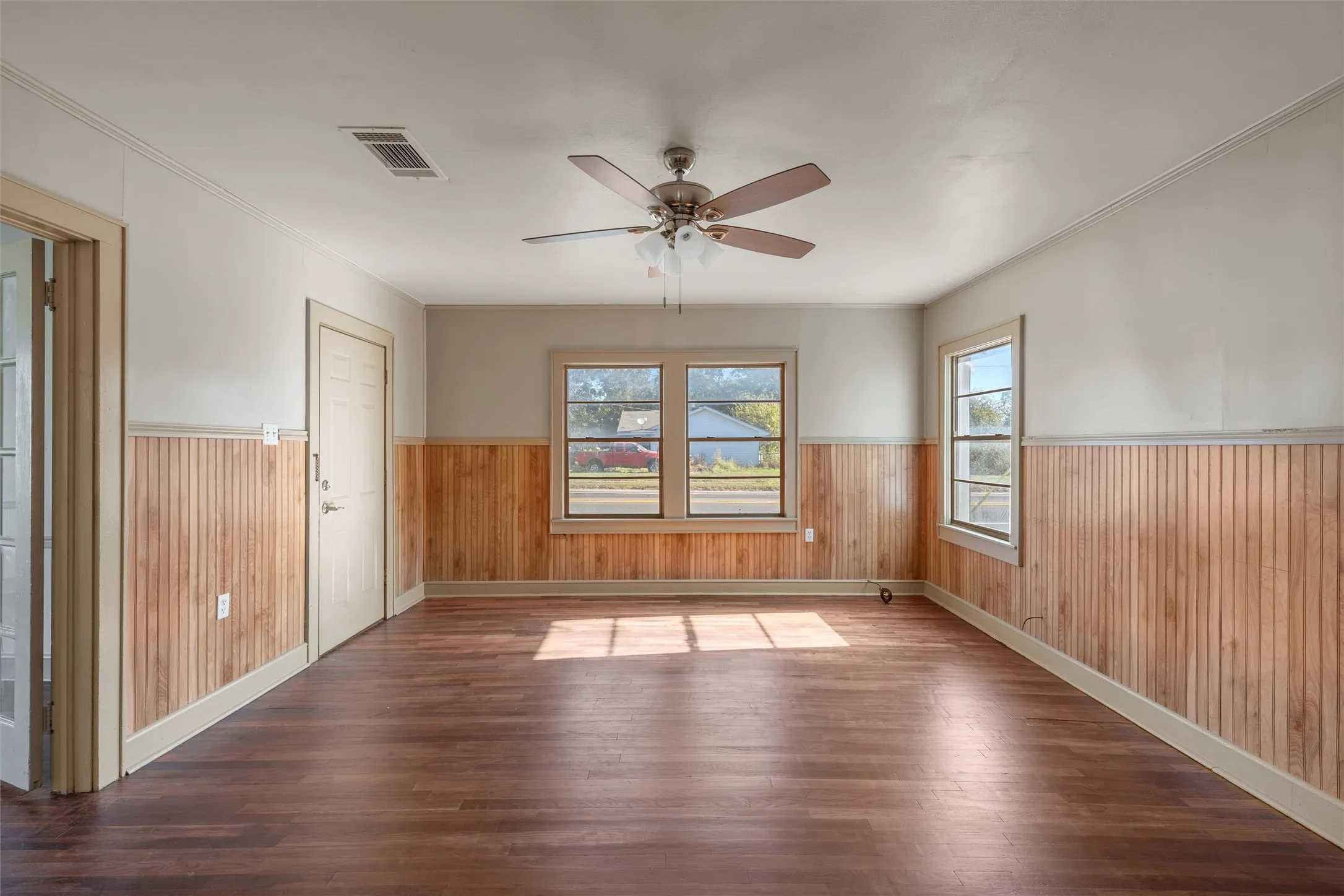Spacious room featuring wood-finish flooring, beadboard wall paneling, and a ceiling fan