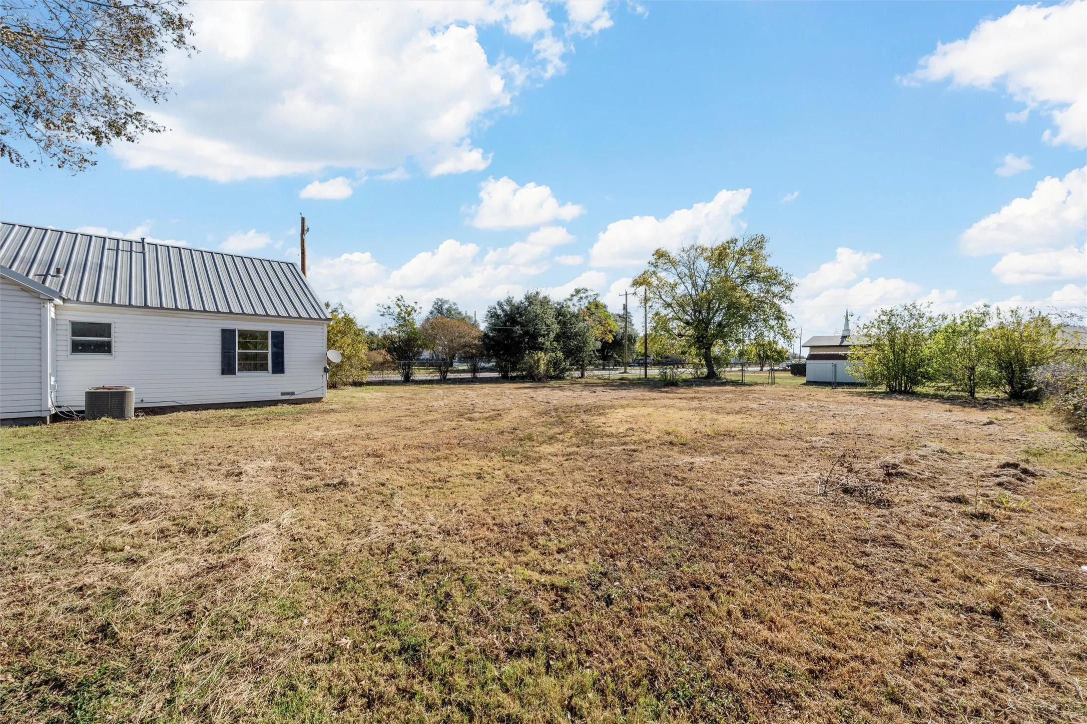 Expansive outdoor space featuring a white siding structure with a metal roof and dark shutters