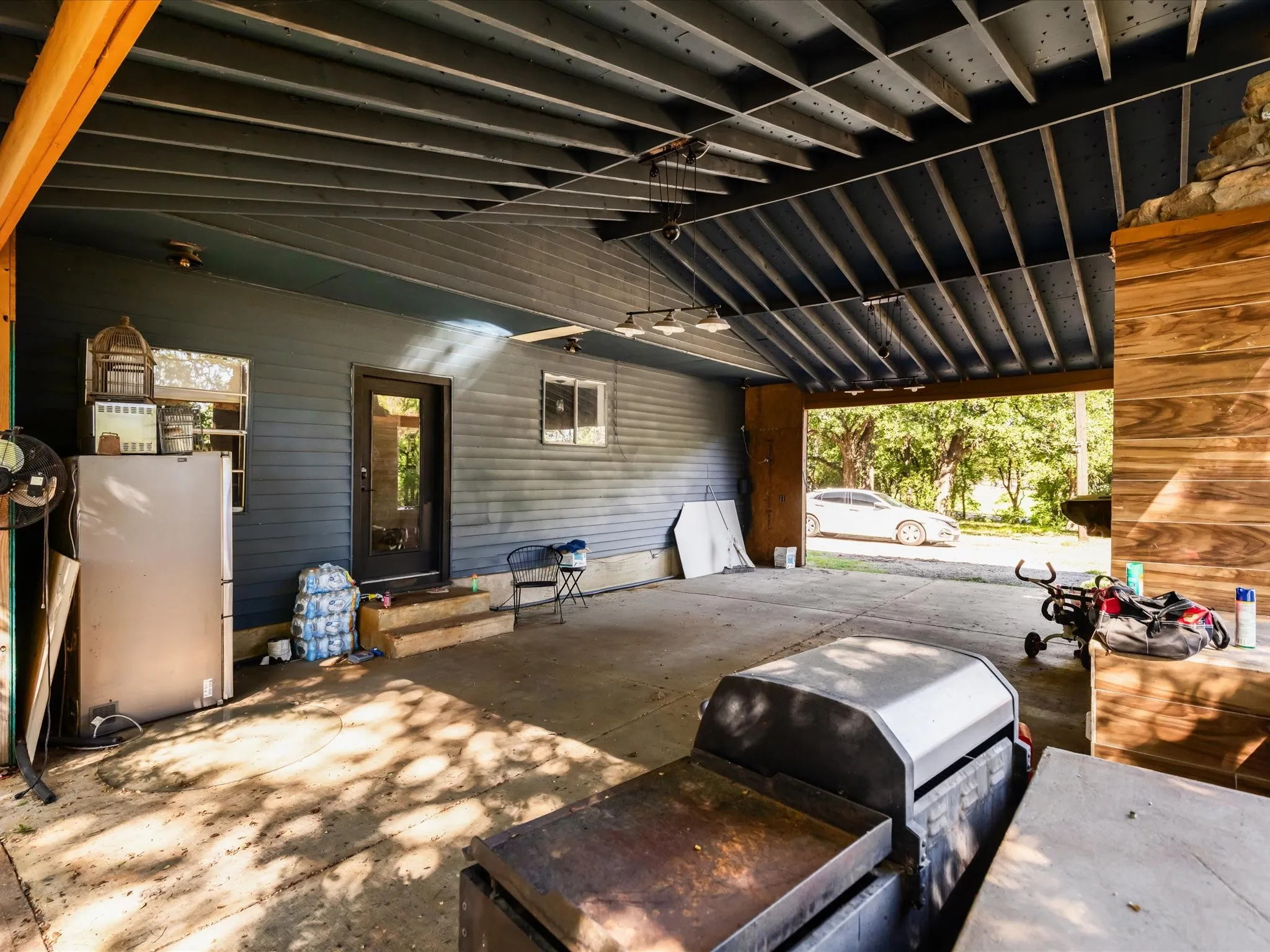 Covered concrete patio area featuring a blue exterior wall with horizontal siding, a glass-paned door, and two windows