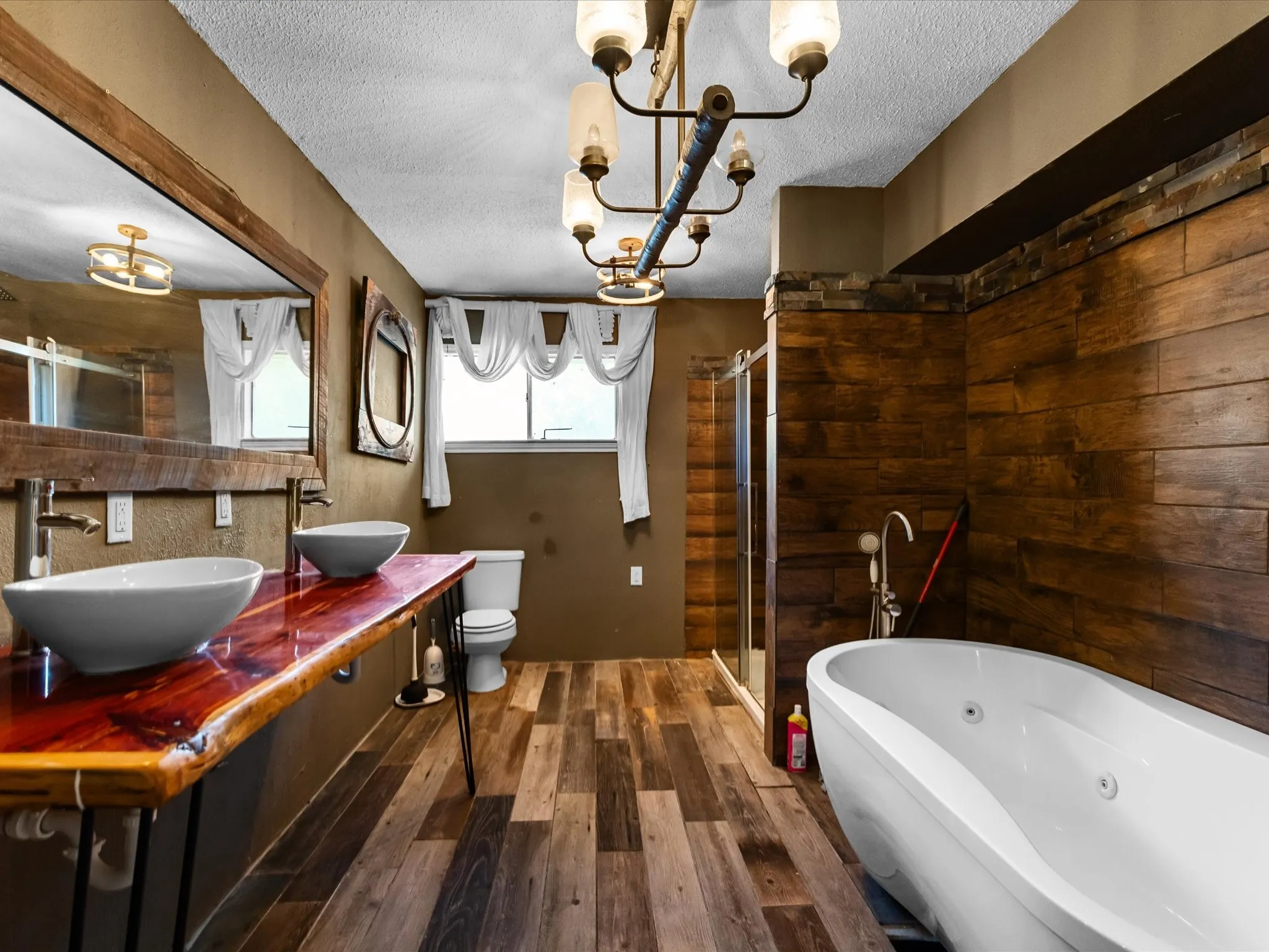Bathroom featuring a live-edge wood vanity with two vessel sinks, a freestanding soaking tub, a glass-enclosed shower, wood-finish flooring, and a multi-light chandelier