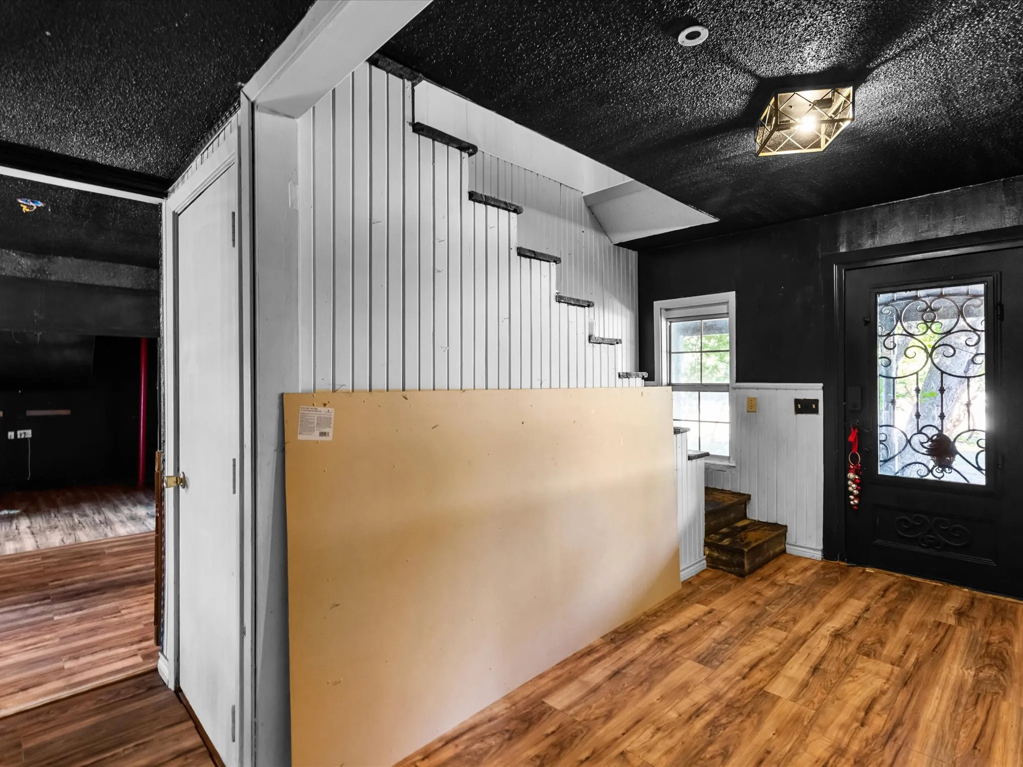 Entryway featuring wood-finish flooring, white vertical wall paneling, and a dark, ornate glass-paneled entry door