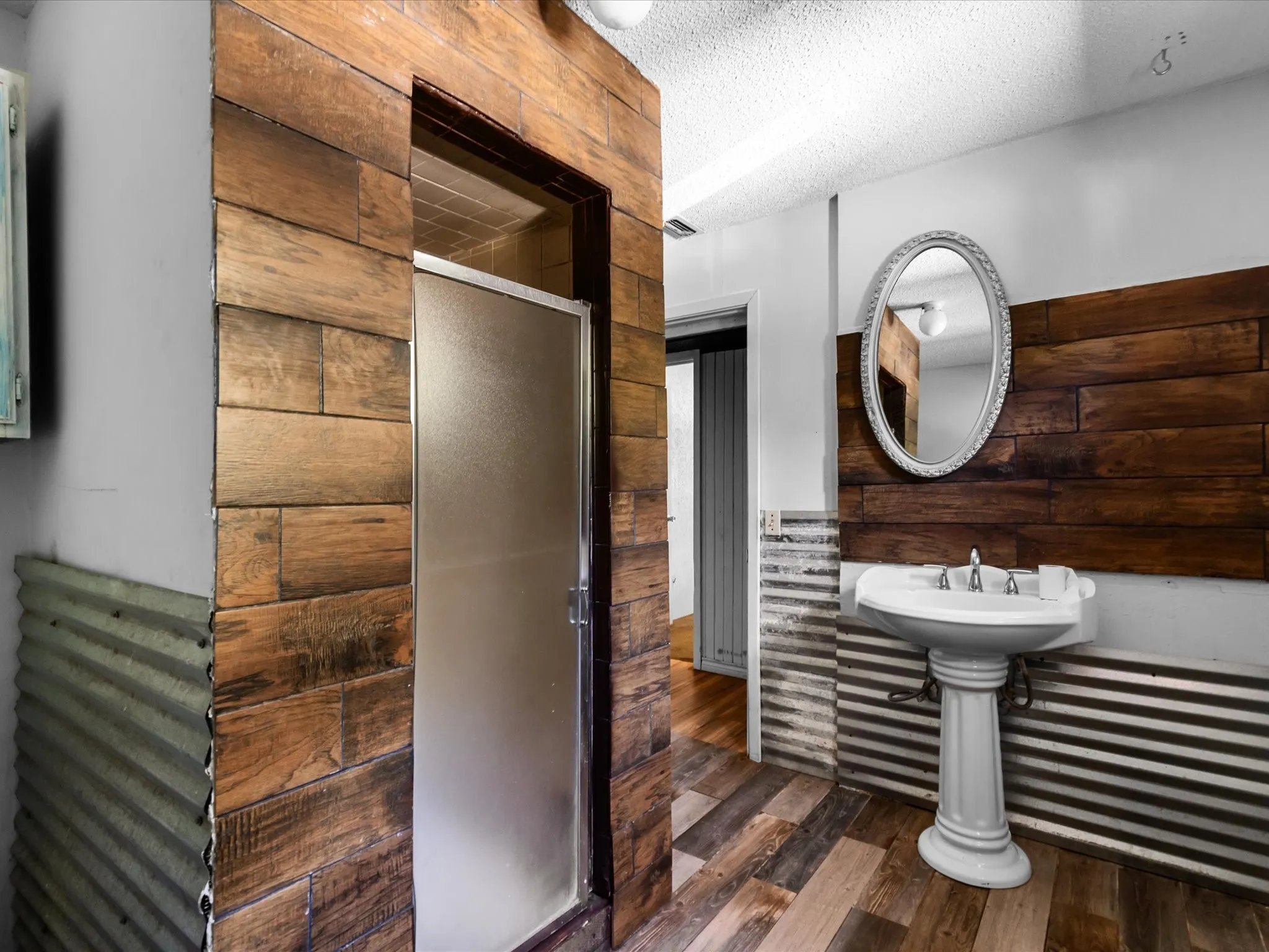 Bathroom featuring a wood-finish accent wall, corrugated metal wainscoting, and a pedestal sink