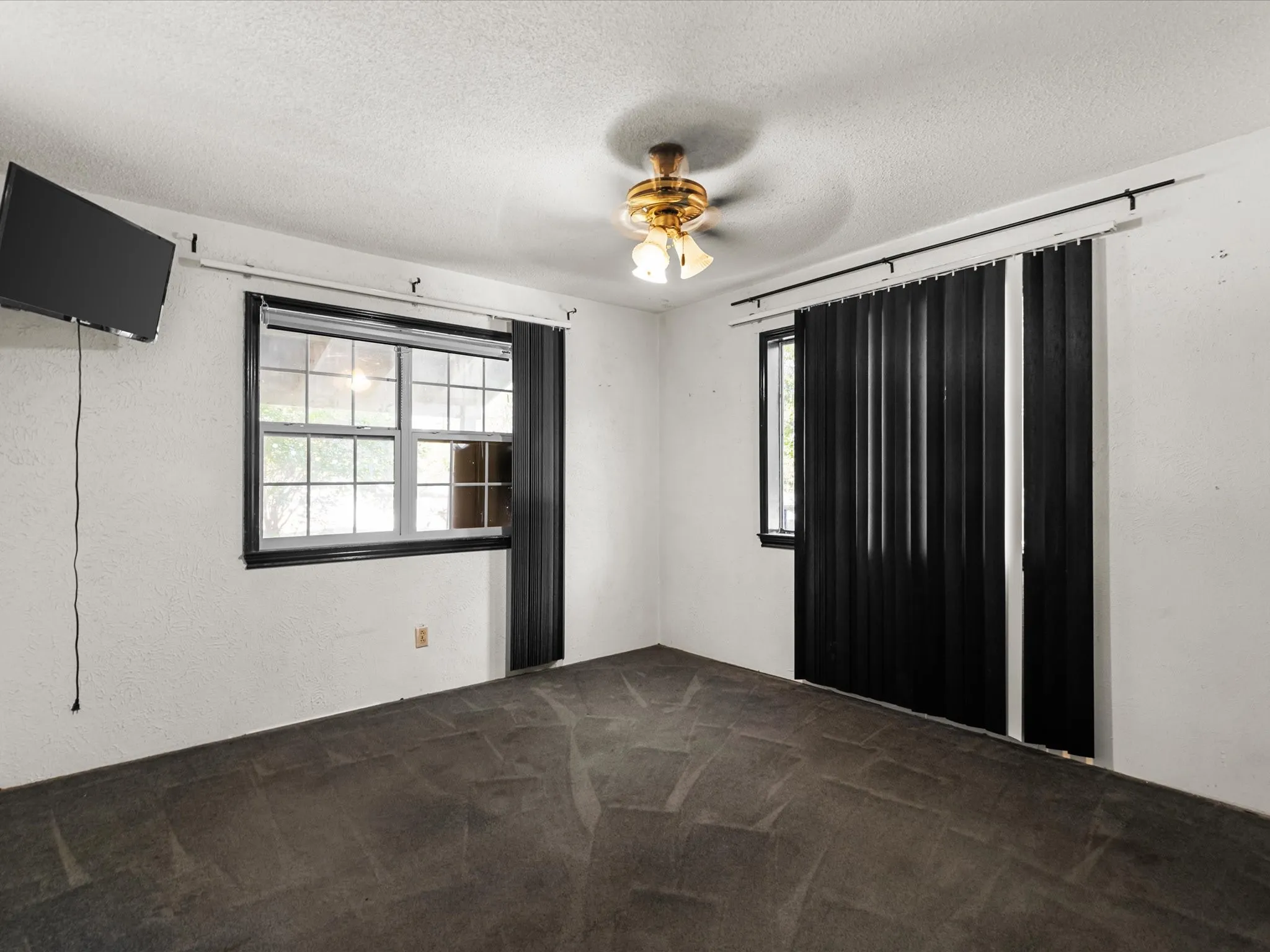 Room featuring textured white walls, dark flooring, and a ceiling fan with integrated lighting