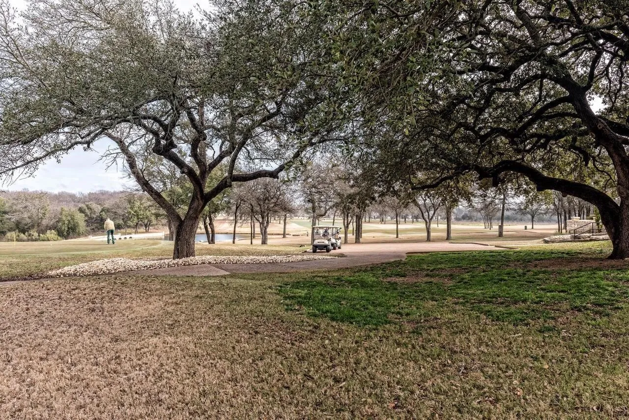 Expansive natural landscape featuring mature trees, a paved pathway, and distant water features