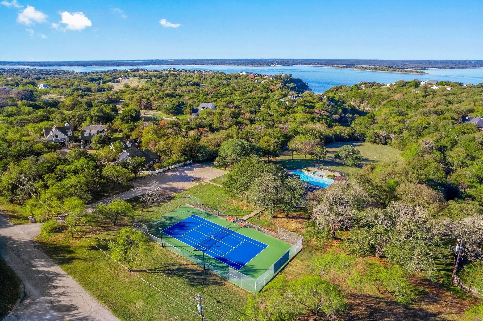Aerial perspective showcasing a tennis court, a freeform swimming pool, and extensive wooded grounds