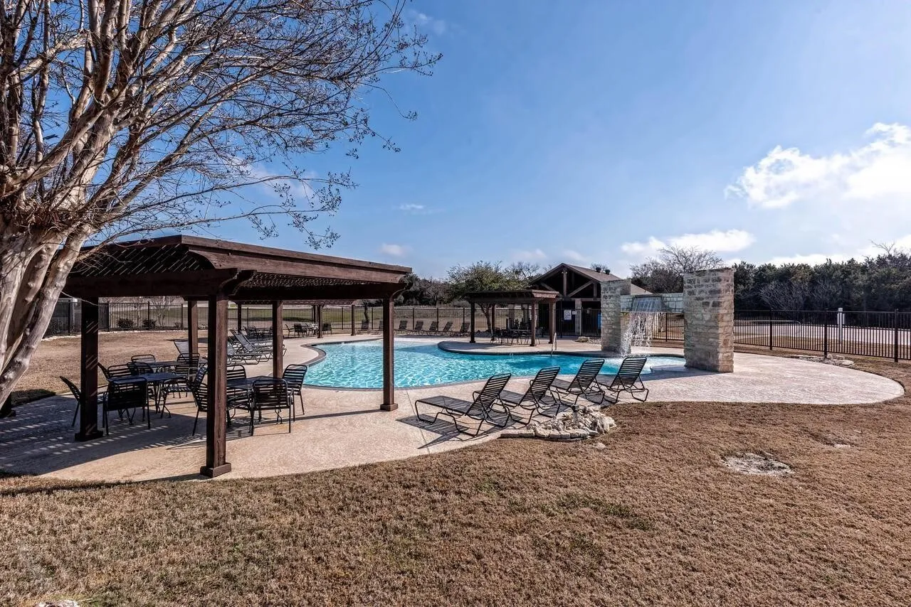 Resort-style pool area featuring a freeform swimming pool, integrated water feature, and extensive concrete decking