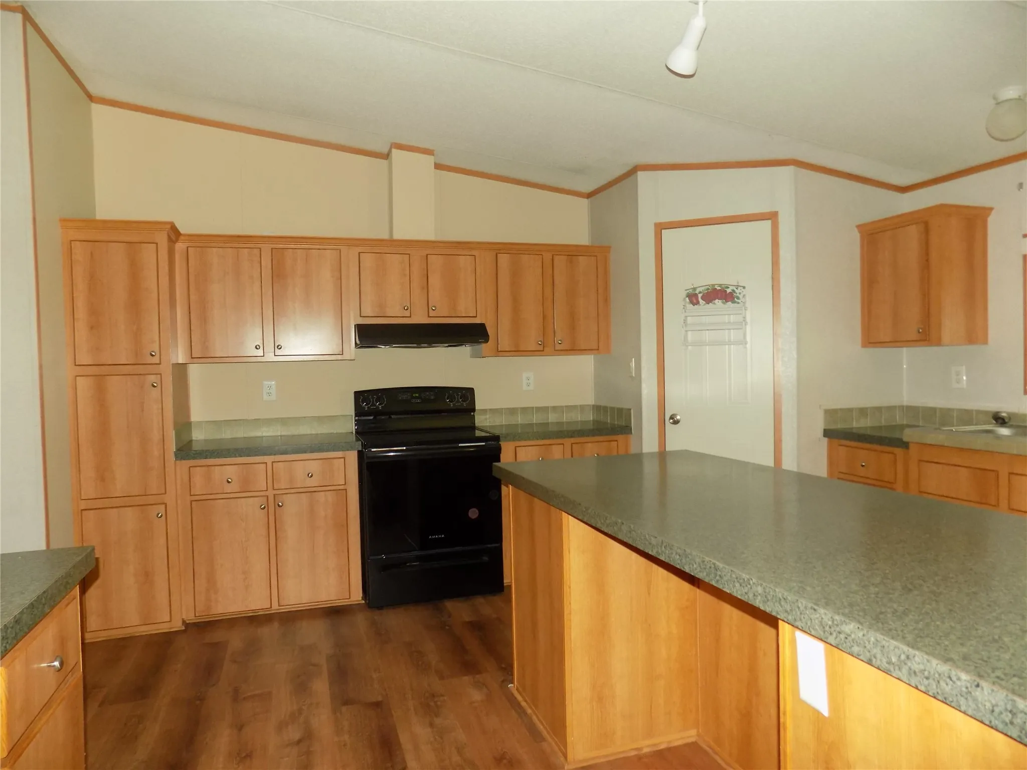 View of open awesome kitchen area, picturing center island, stove, multiple cabinets, and large counter space.