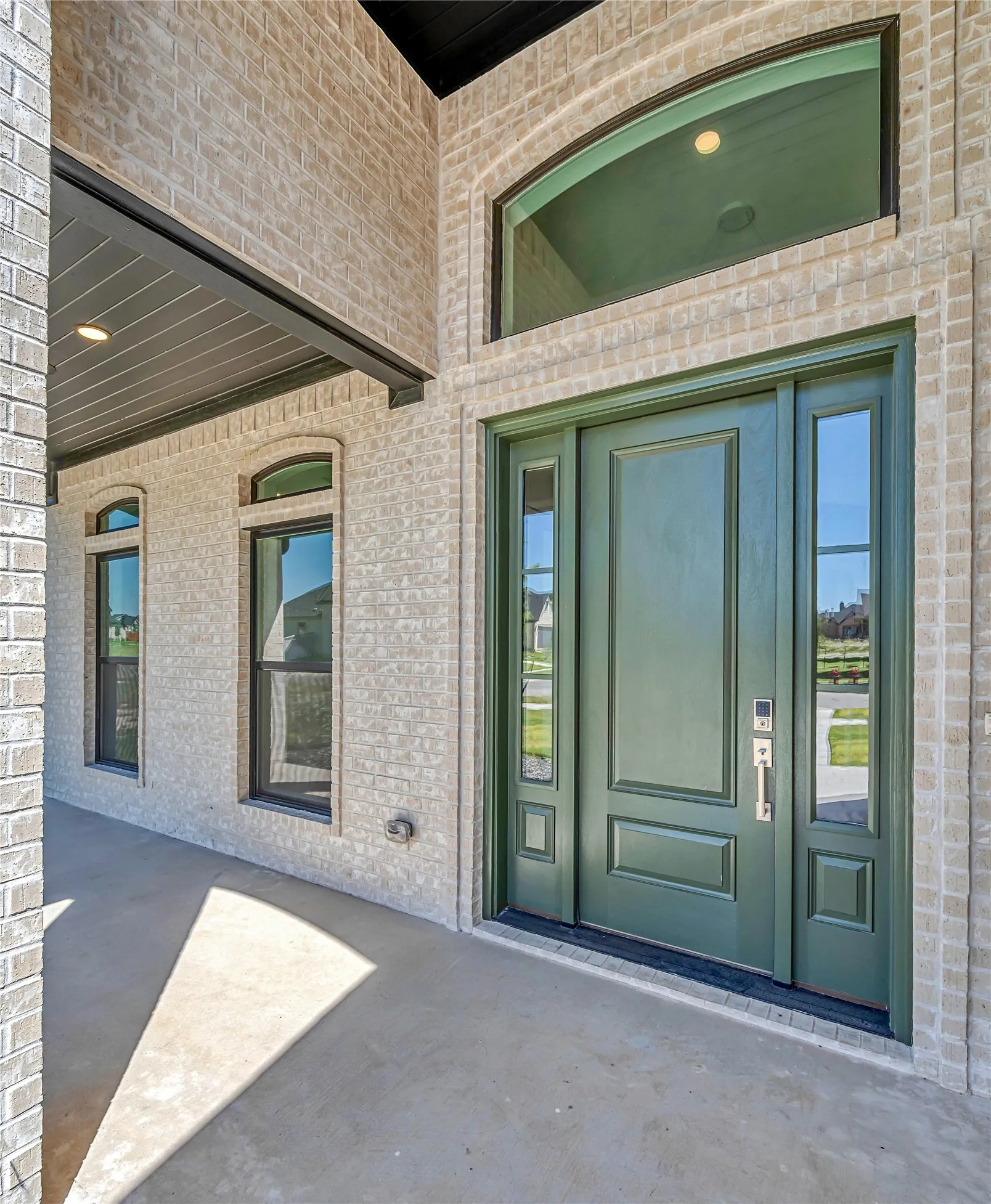 Brick exterior with a prominent green entry door, framed by sidelight windows and an arched transom window