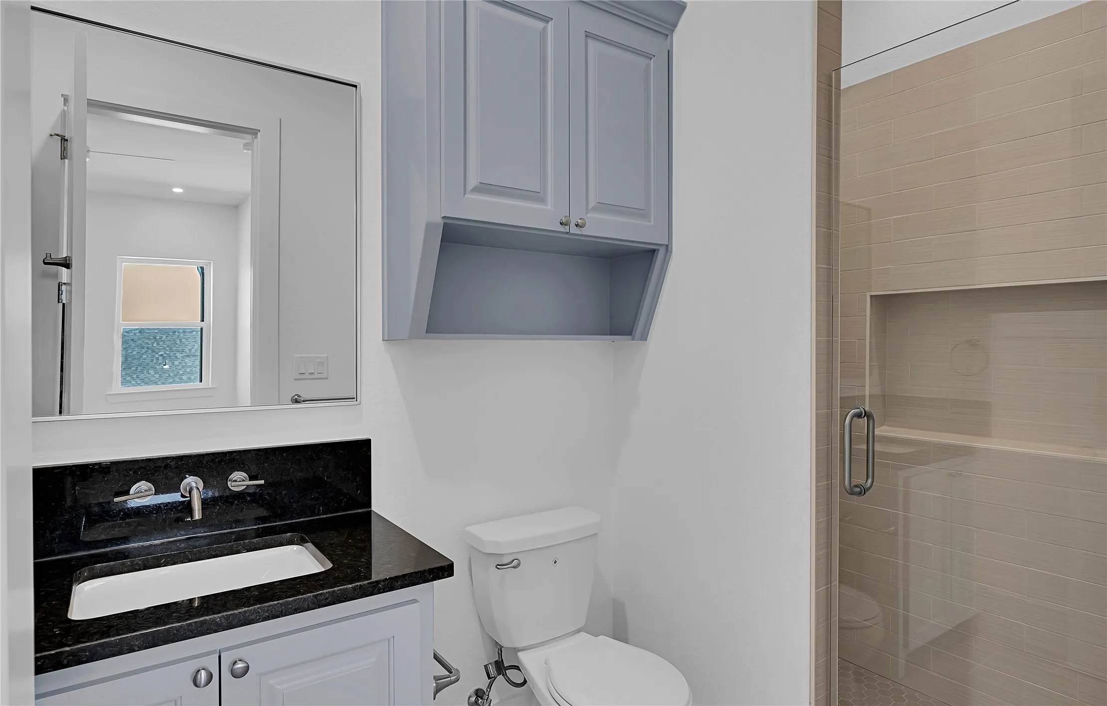 Bathroom featuring a shower with light-toned rectangular wall tiles and a built-in niche, a glass enclosure, and a vanity with a black countertop and an undermount sink