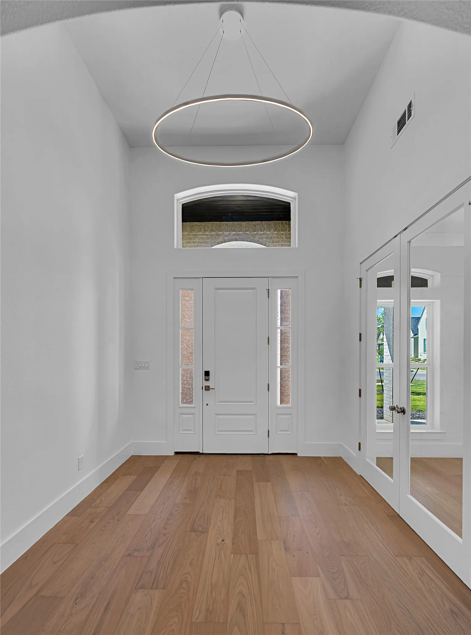 Two-story entryway featuring a modern circular chandelier, wood-finish flooring, white baseboards, and a transom window above the main entry door
