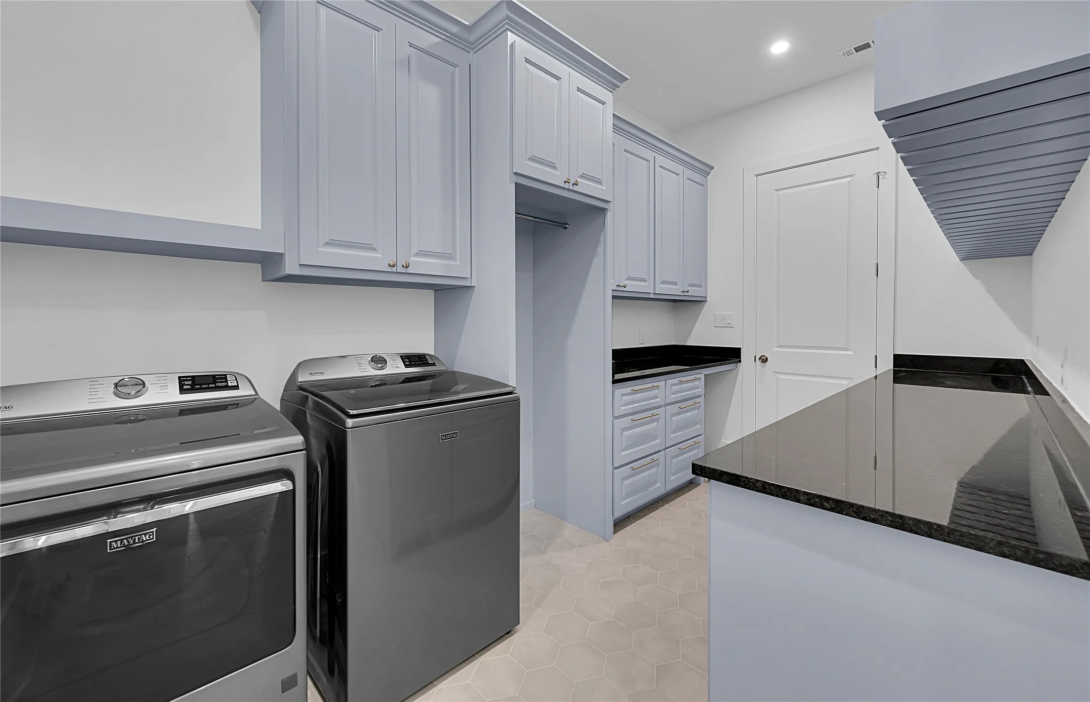 Laundry room featuring light gray cabinetry, dark stone countertops, hexagon tile flooring, and built-in shelving