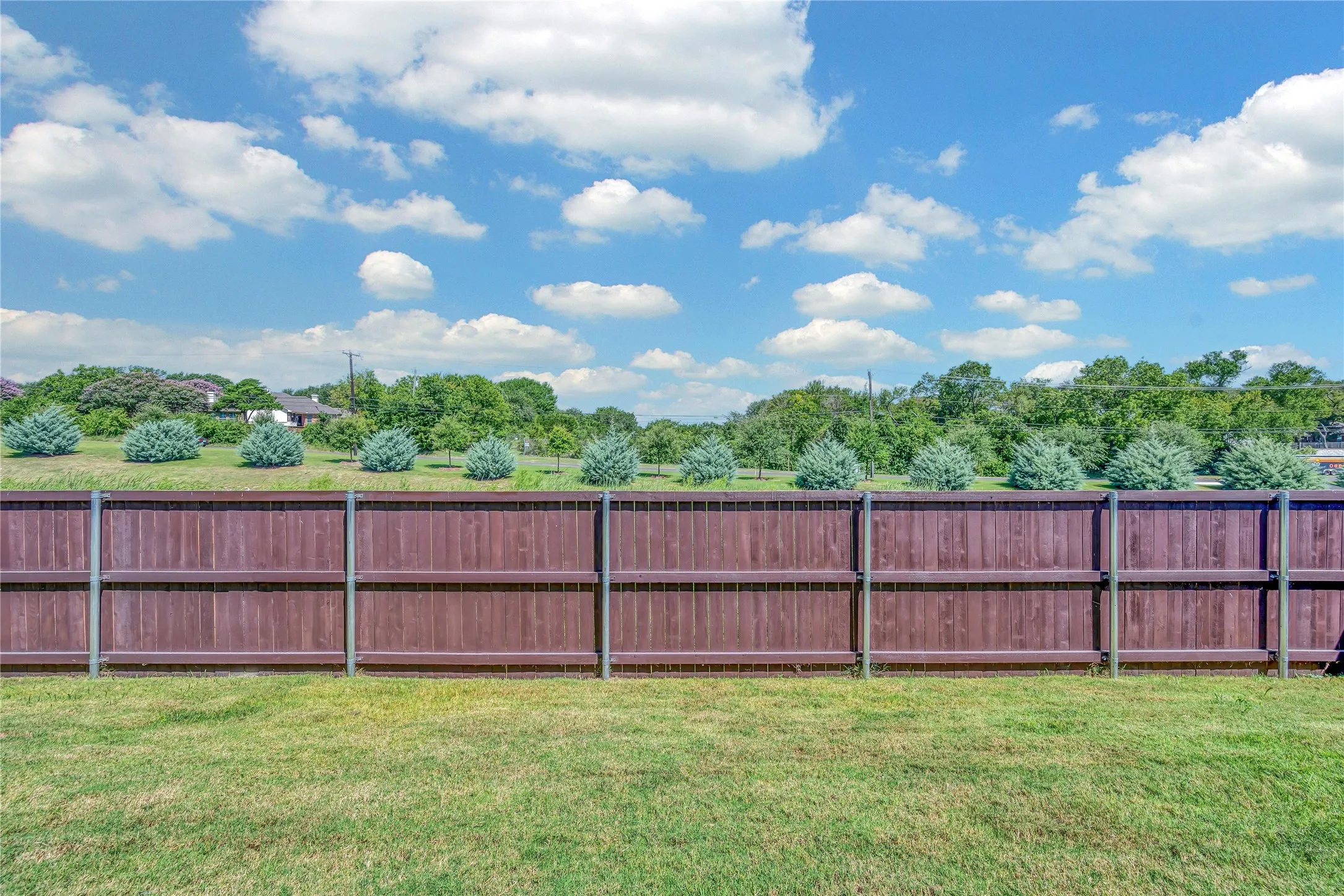 Expansive backyard featuring a manicured lawn, a stained wood privacy fence with metal posts, and lush green landscaping with ornamental shrubs