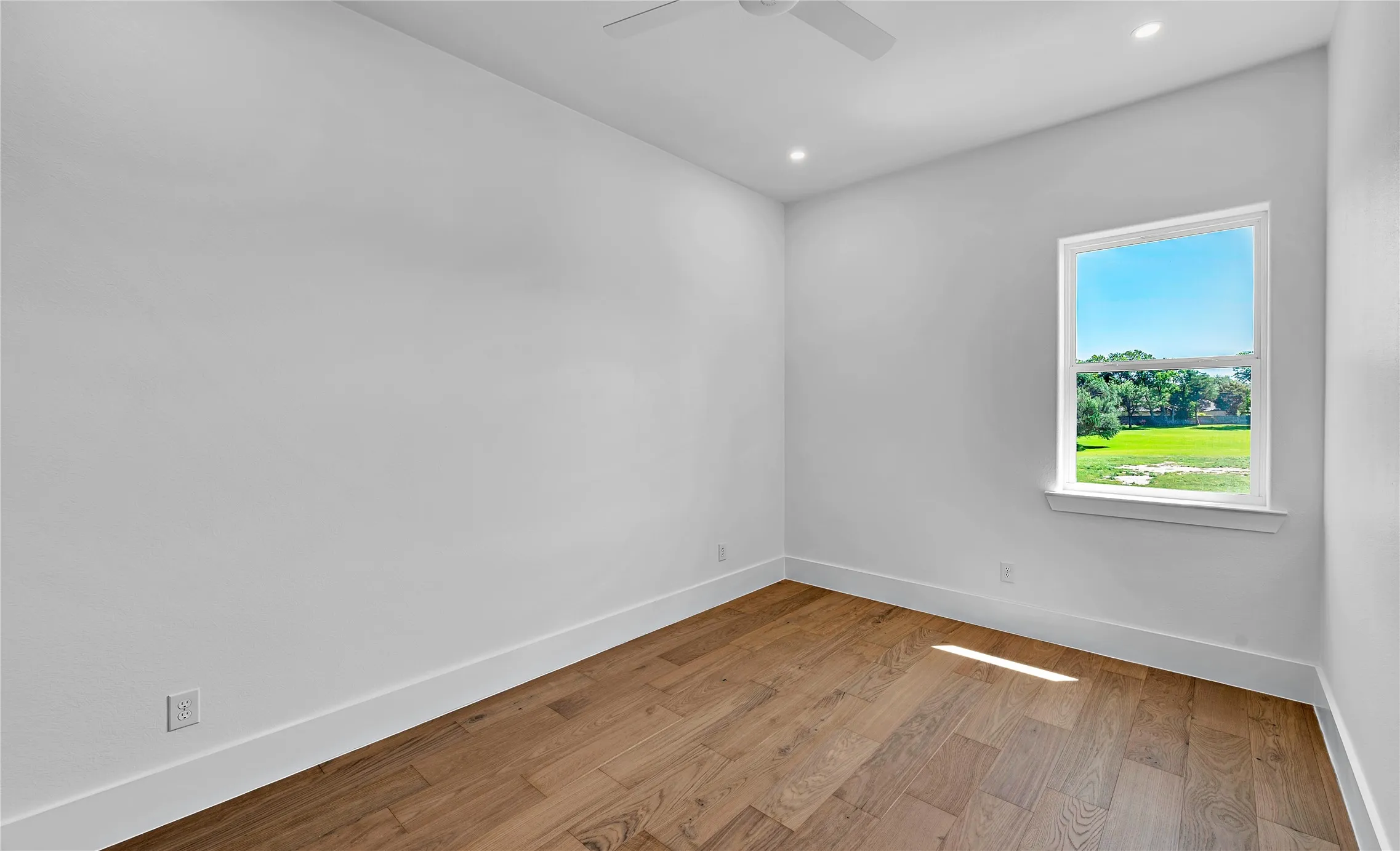 Spacious room featuring wood-finish flooring, white baseboards, and a large window with white trim