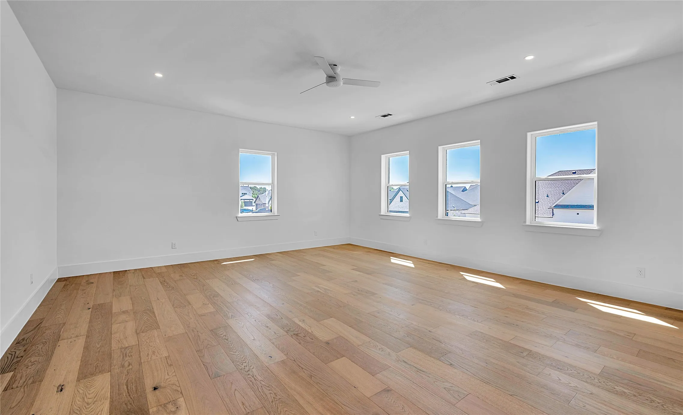 Spacious room featuring wood-finish flooring, white walls, and multiple windows