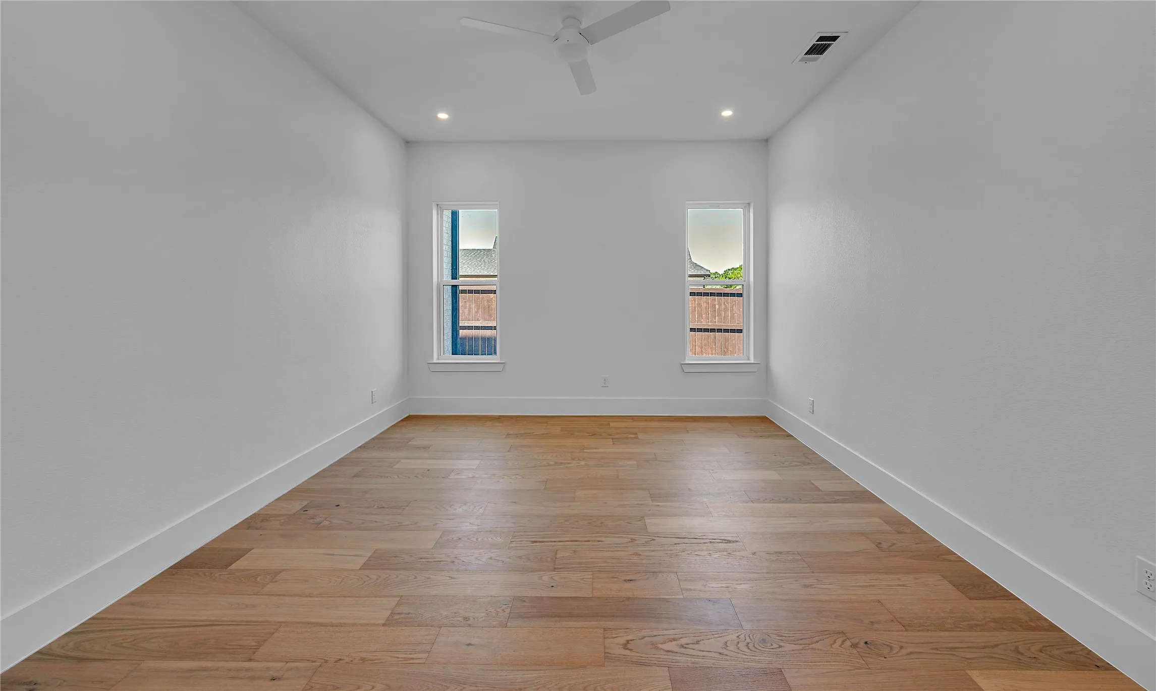 Spacious interior room featuring wood-finish flooring, two windows, recessed lighting, and a ceiling fan