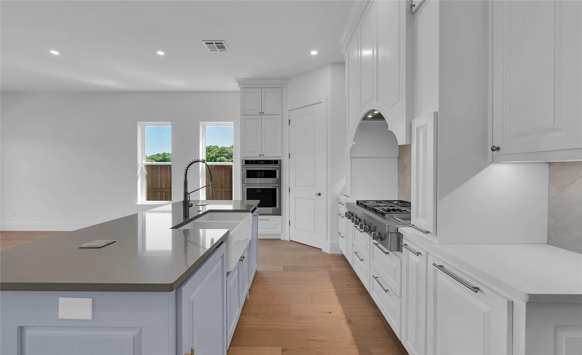 Kitchen featuring a large island with a farmhouse sink, stainless steel appliances, light wood-finish flooring, white cabinetry, and recessed lighting