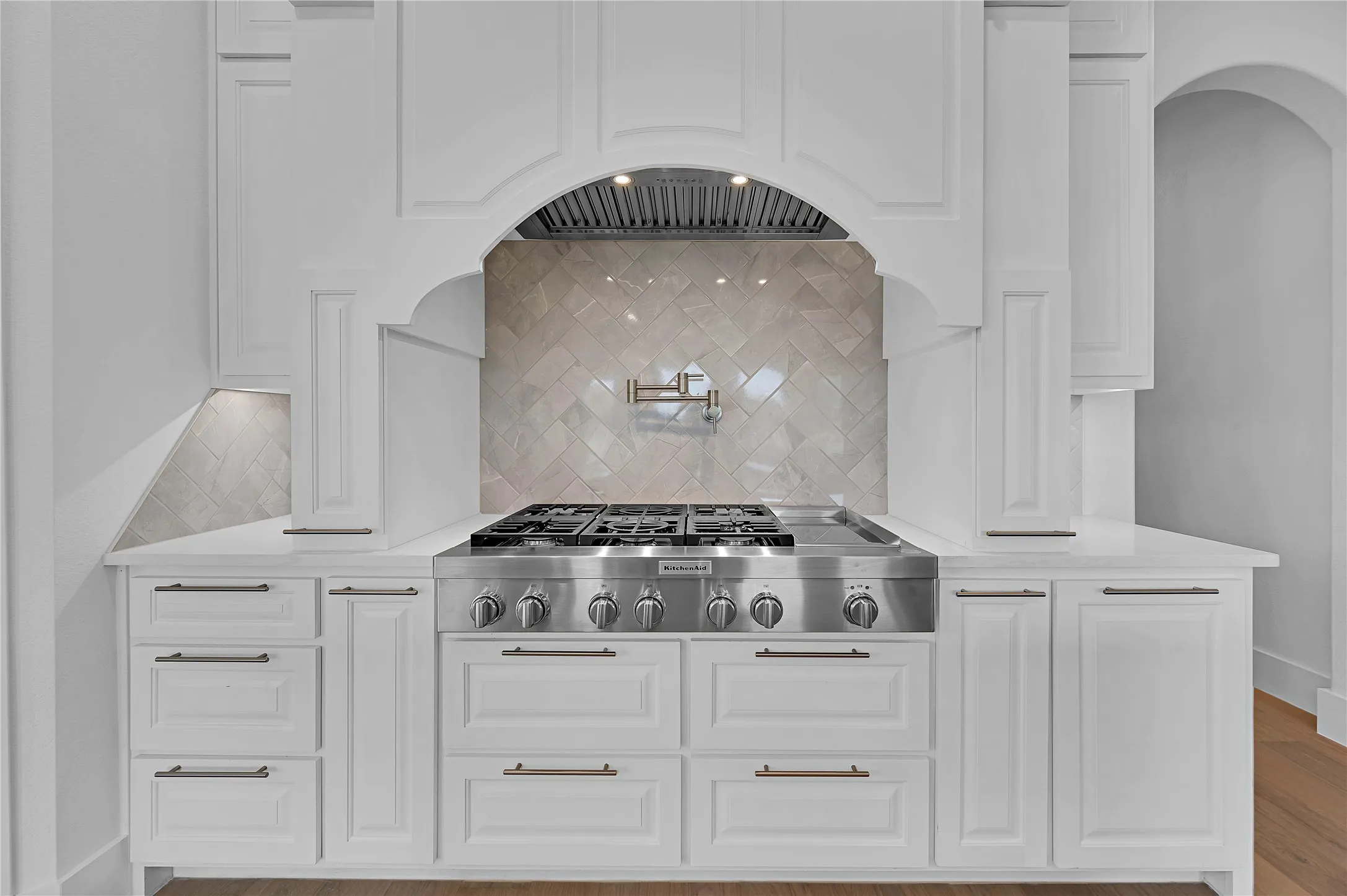 Professional-grade stainless steel range with a pot filler faucet, set within white cabinetry, under an arched range hood