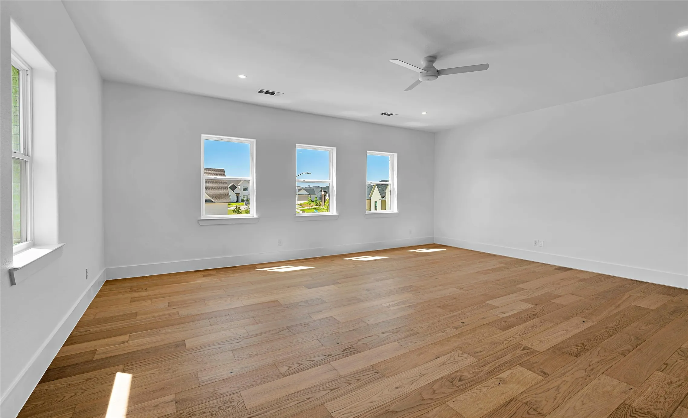 Spacious room featuring wood-finish flooring, white walls, and multiple windows