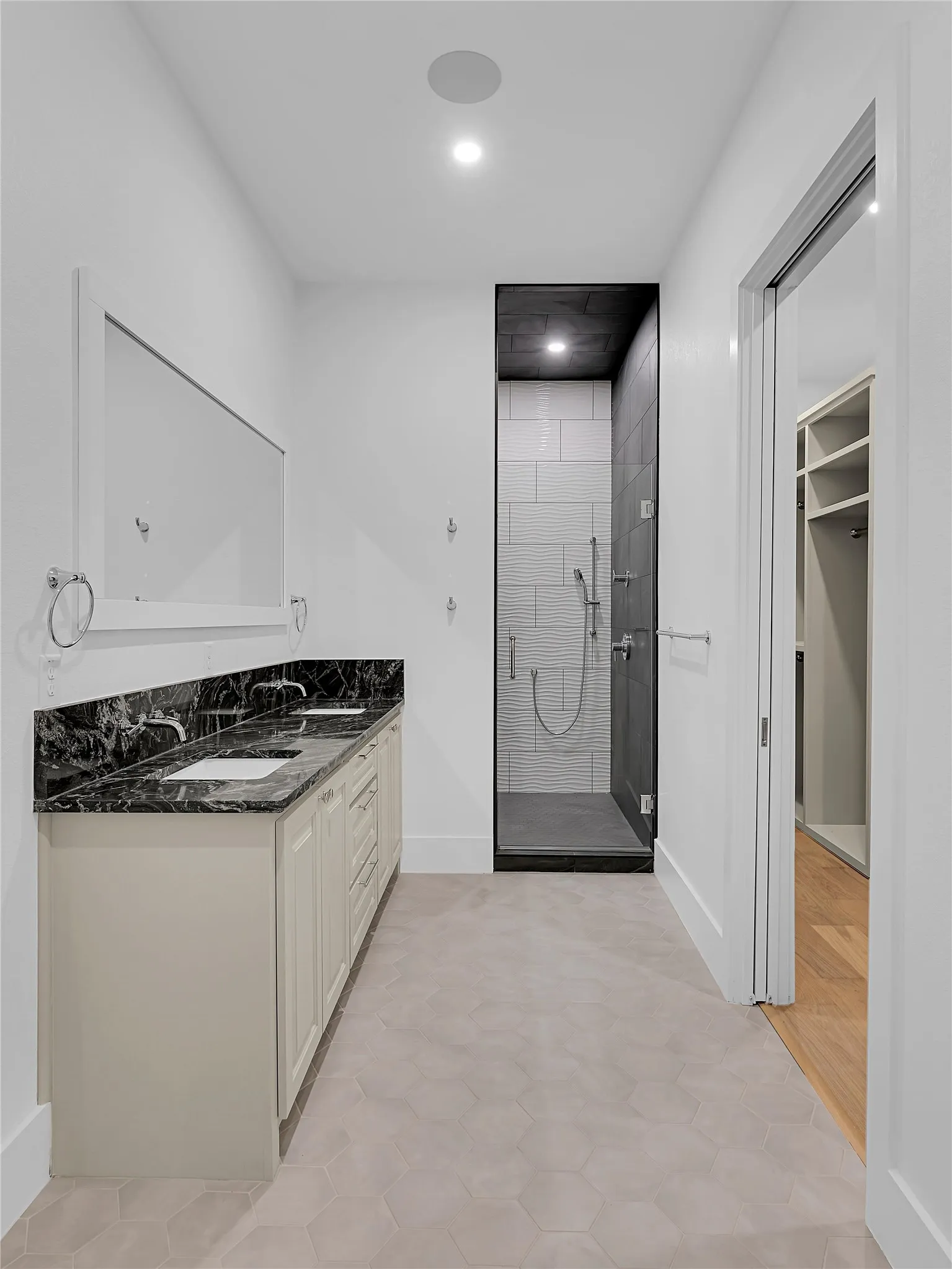 Bathroom featuring a dual vanity with a dark marbled countertop, hexagonal floor tiling, a walk-in shower with subway-style wall tiles, and recessed lighting