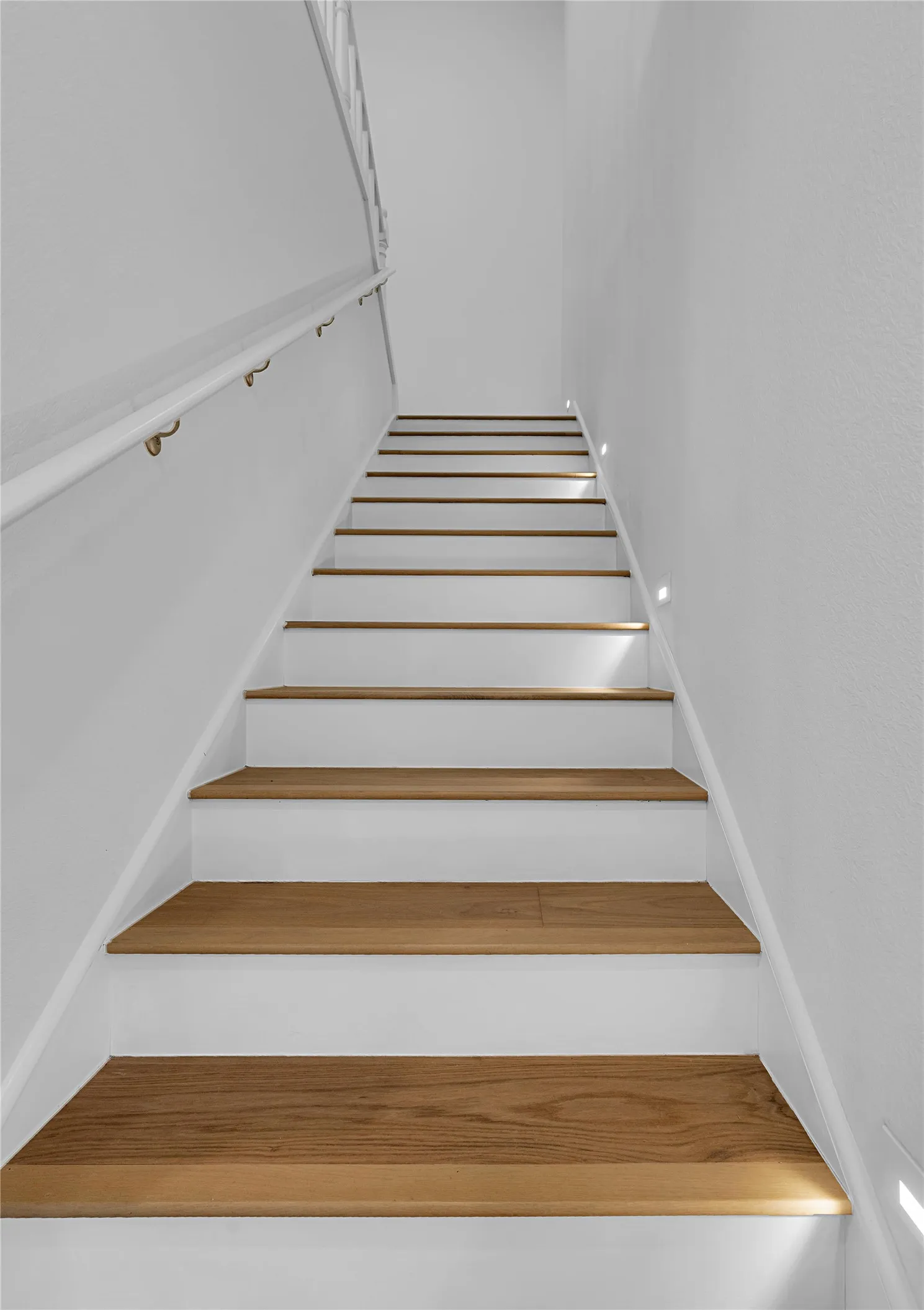 Staircase featuring wood-finish treads, white risers, and a white handrail with brass-finish brackets