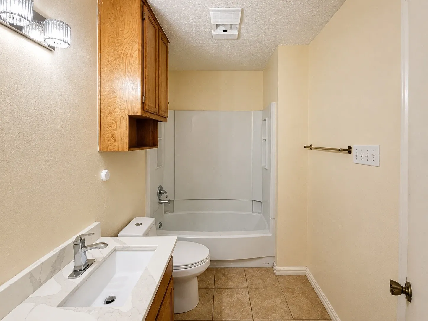 Bathroom featuring a white bathtub/shower combination, tile flooring, and a vanity with a white countertop and integrated sink