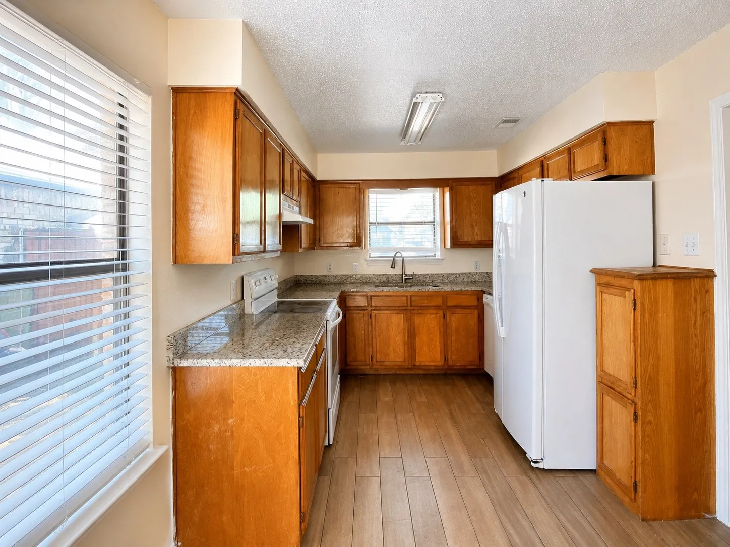 Kitchen featuring wood-finish flooring, wood cabinetry, granite countertops, and a stainless steel sink with a gooseneck faucet