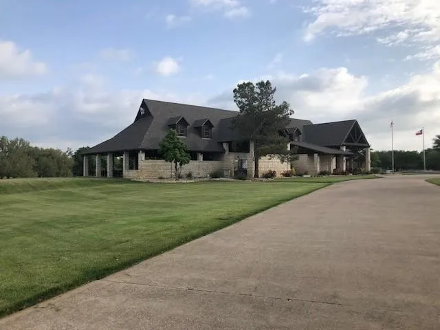 Stone-clad property with a dark shingled roof, multiple dormer windows, a columned covered patio, and a wide paved driveway
