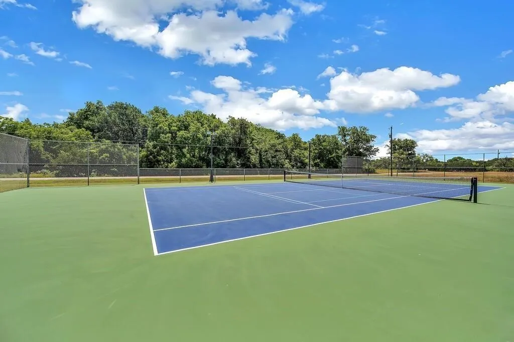 Regulation-sized tennis court featuring a blue playing surface and green surrounding area