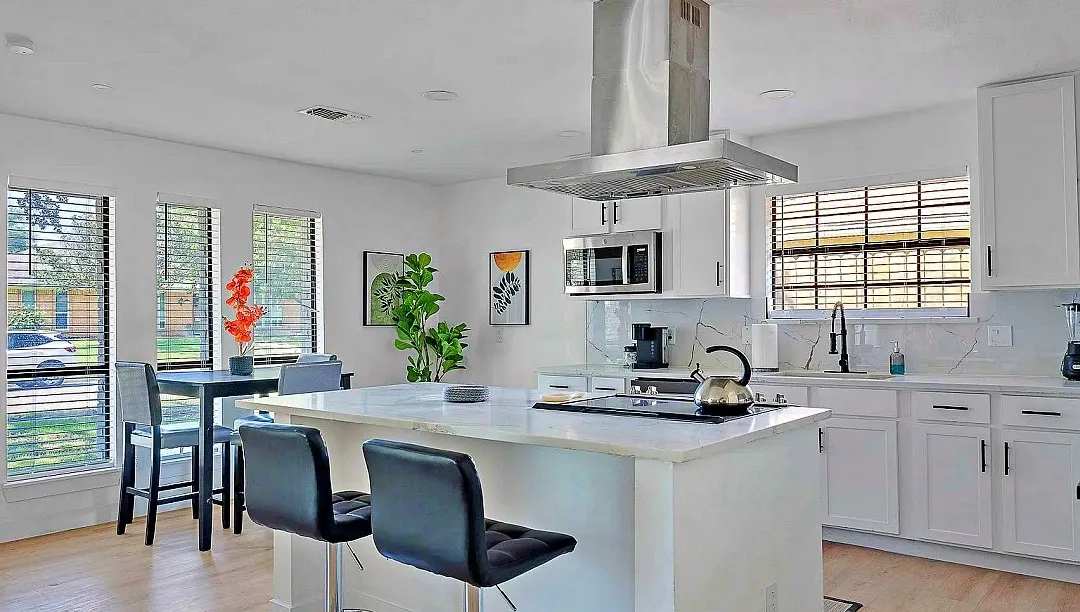 Modern kitchen featuring a central island with integrated cooktop, white cabinetry, stainless steel appliances, and wood-finish flooring