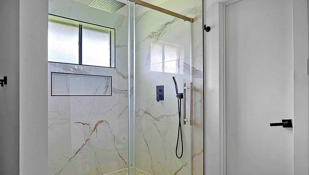 Glass-enclosed shower featuring large format veined wall tiles, a built-in shower niche, a window with frosted glass, and a matte black shower system with a handheld sprayer