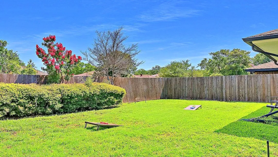 Expansive backyard featuring a manicured lawn, a full privacy fence, and mature landscaping with flowering trees and hedges