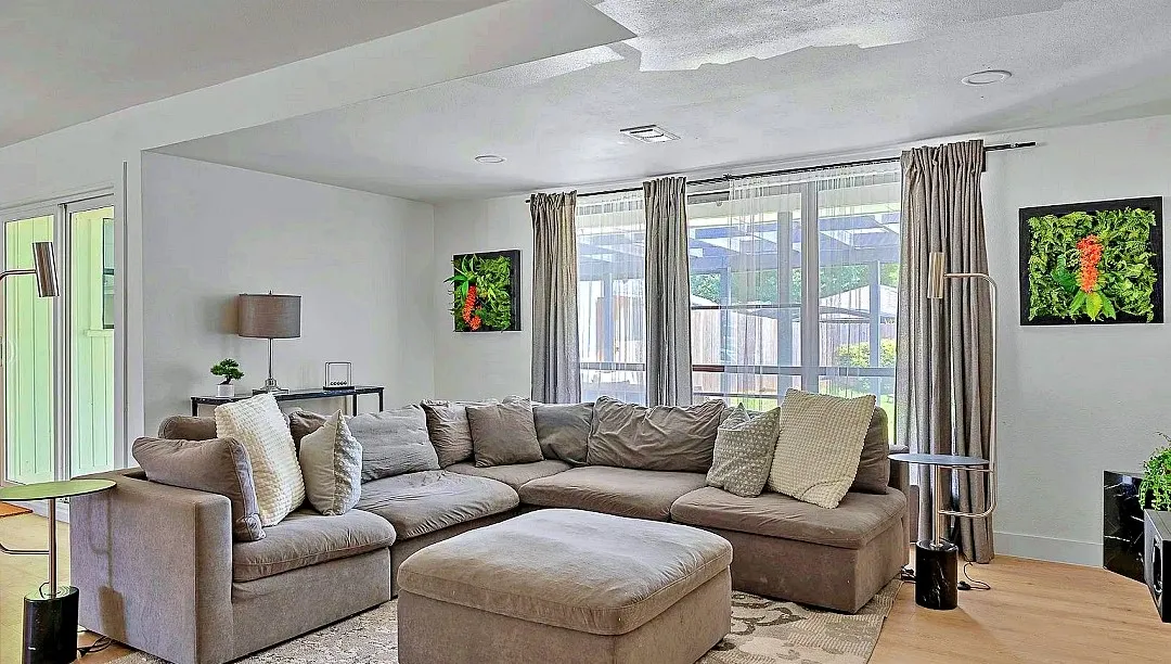 Spacious living area featuring light wood-finish flooring, recessed lighting, and large windows with privacy drapes