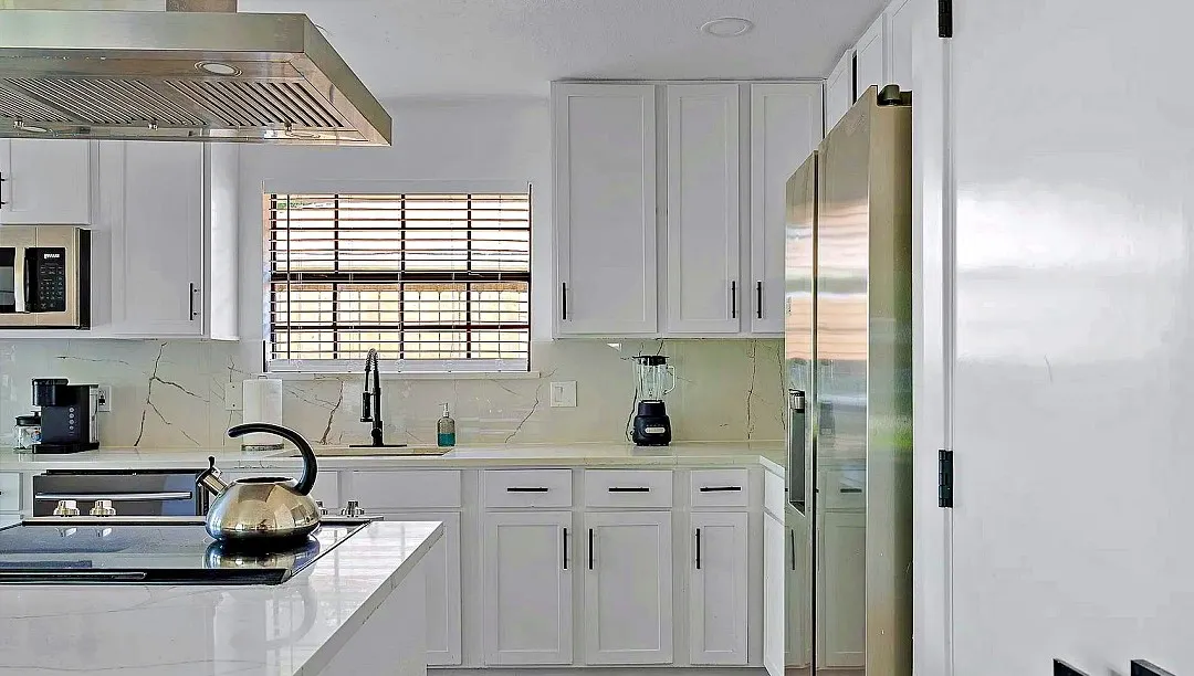 Modern kitchen featuring white cabinetry, a stainless steel range hood, stone countertops, integrated cooktop, and stainless steel appliances