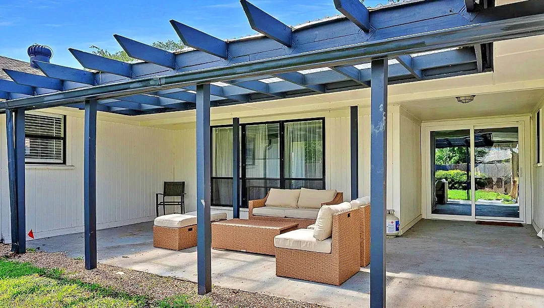 Expansive concrete patio featuring a dark-toned pergola, providing covered outdoor living space