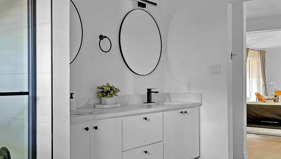 Bathroom vanity featuring a light countertop, white cabinetry with black hardware, and two round mirrors with black frames