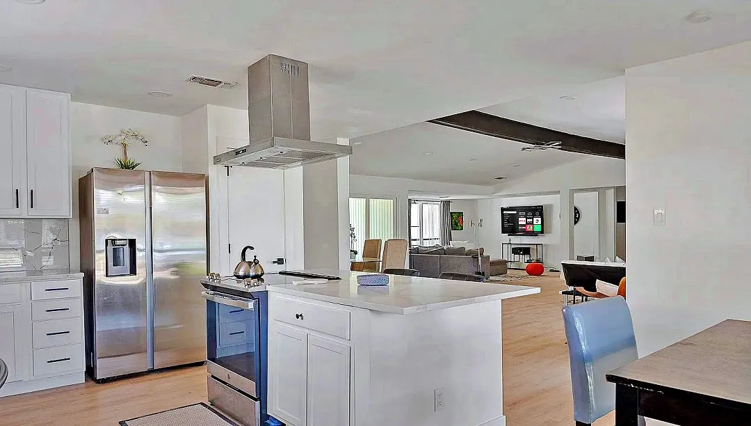 Open-concept kitchen featuring an island, white cabinetry, stainless steel appliances, and wood-finish flooring