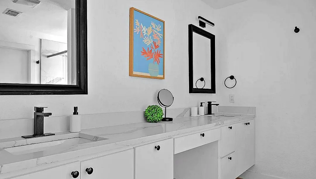 Dual vanity bathroom featuring stone-finish countertops with integrated sinks, black finish faucets, and white cabinetry